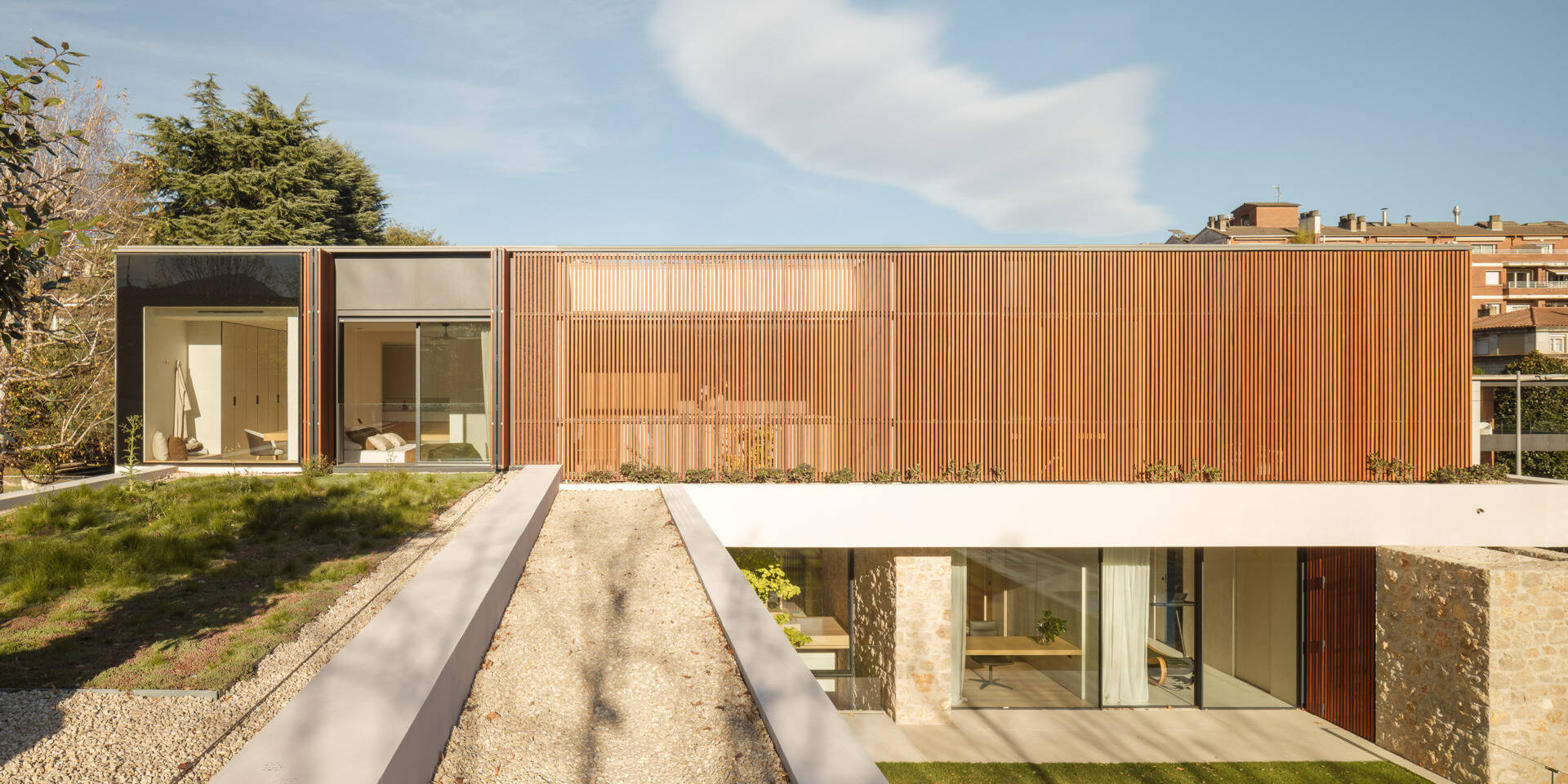 Vertical wooden shutters filter light and views around the upper floor of House 2194 in Olot, Spain. A planted roof adds greenery outside the private rooms of this home by Nordest Architecture SLP.