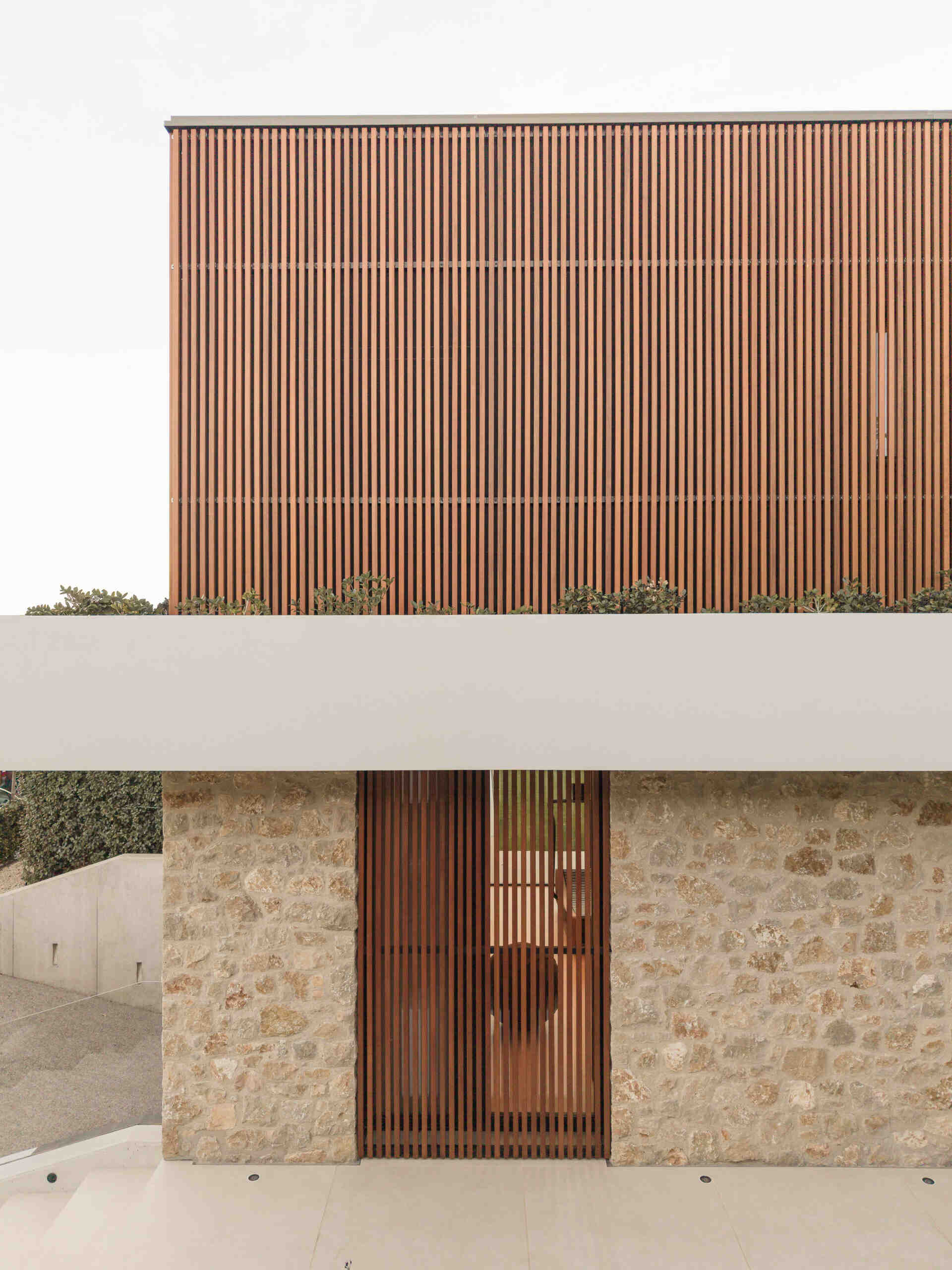 Stone walls, wooden screens, and a projecting concrete slab define this contemporary home in Olot, Spain. Explore House 2194 by Nordest Architecture SLP, with an L-shaped layout, a sheltered garden, and a layered façade.