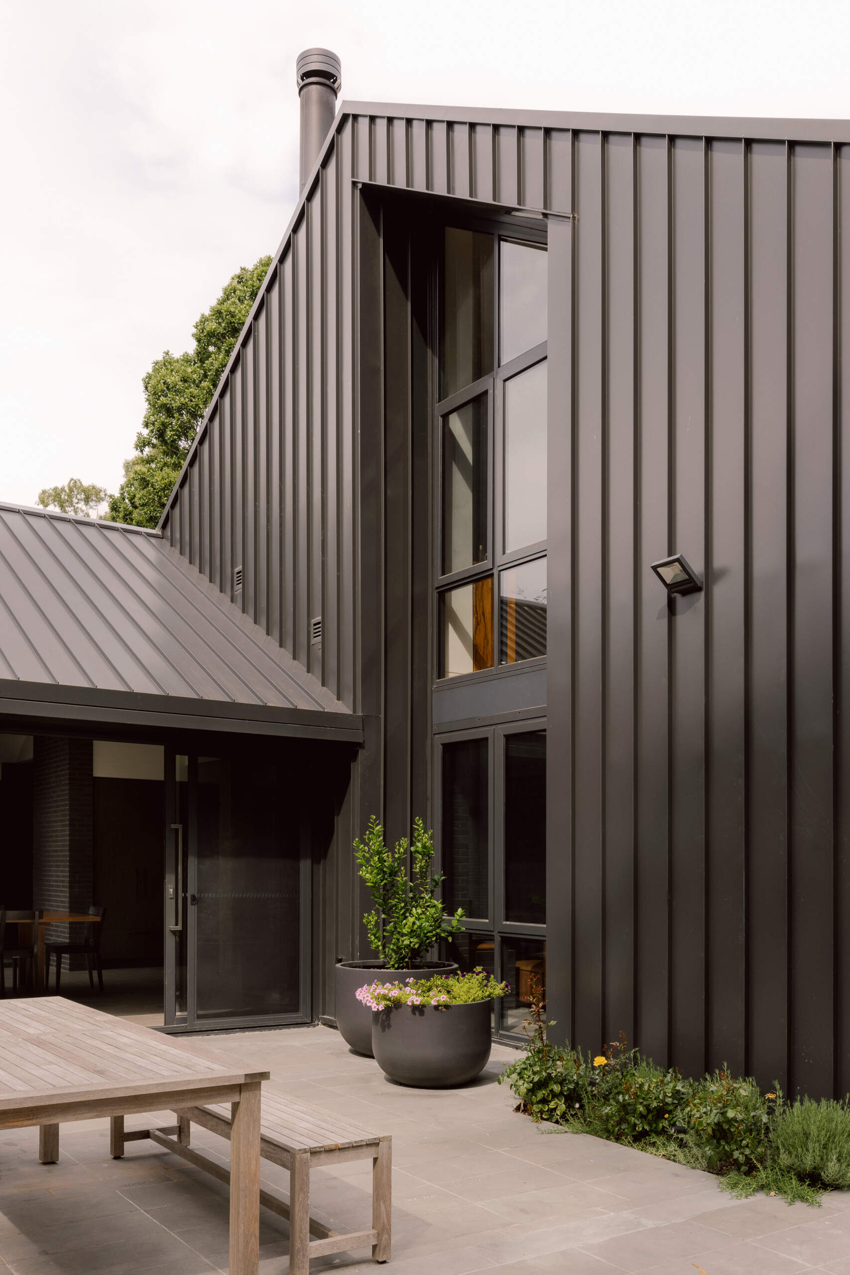 The home's relationship with the landscape continues through its generous areas of glazing and open spaces. A patio furnished with a dining table, and a nearby firepit area, create a casual place to relax outdoors.