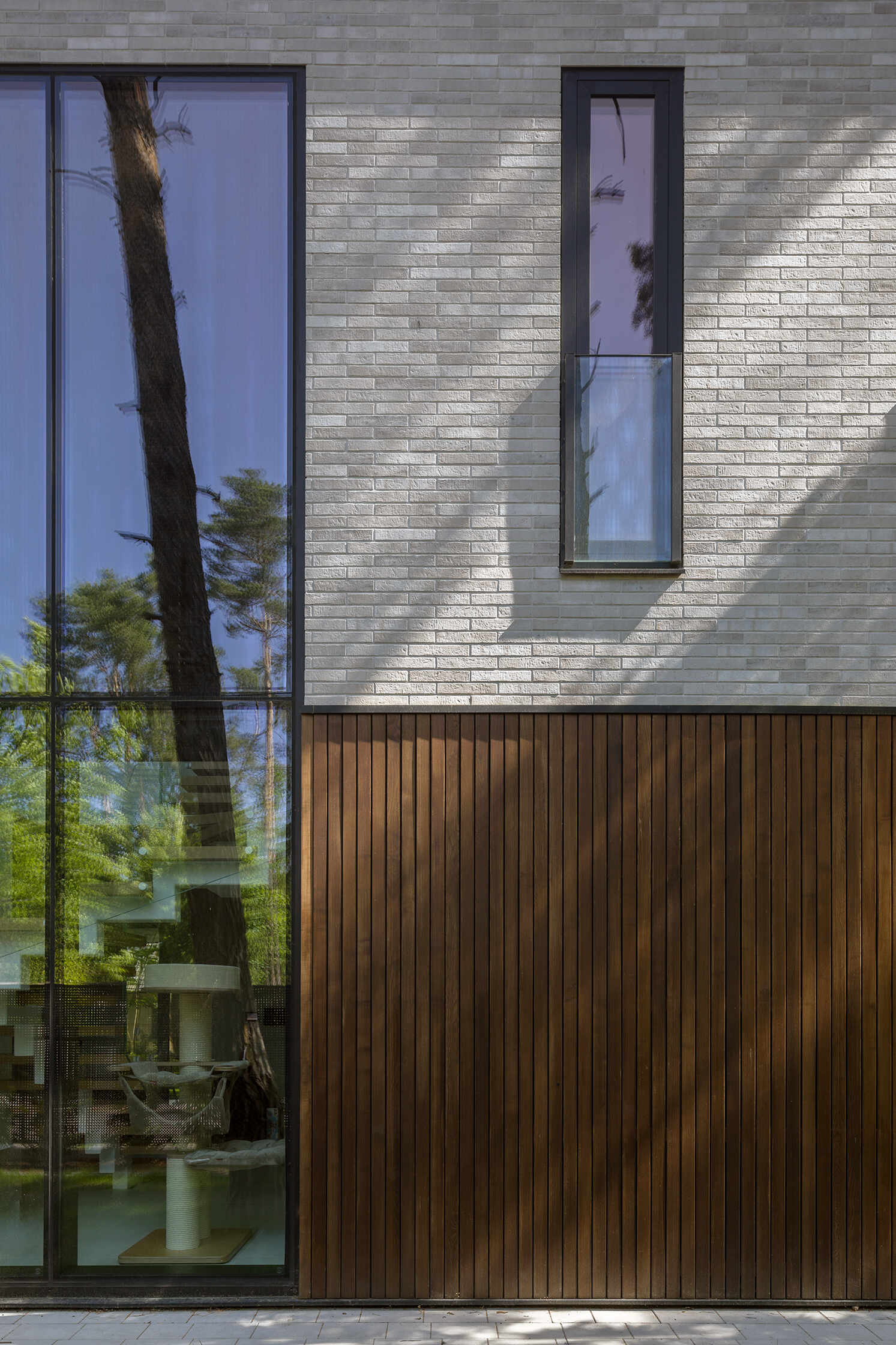 Expansive horizontal glazing and tall vertical windows bring daylight and views of the surrounding pine trees into The Intersecting House near Warsaw, with large living room glazing opening directly onto the terrace.