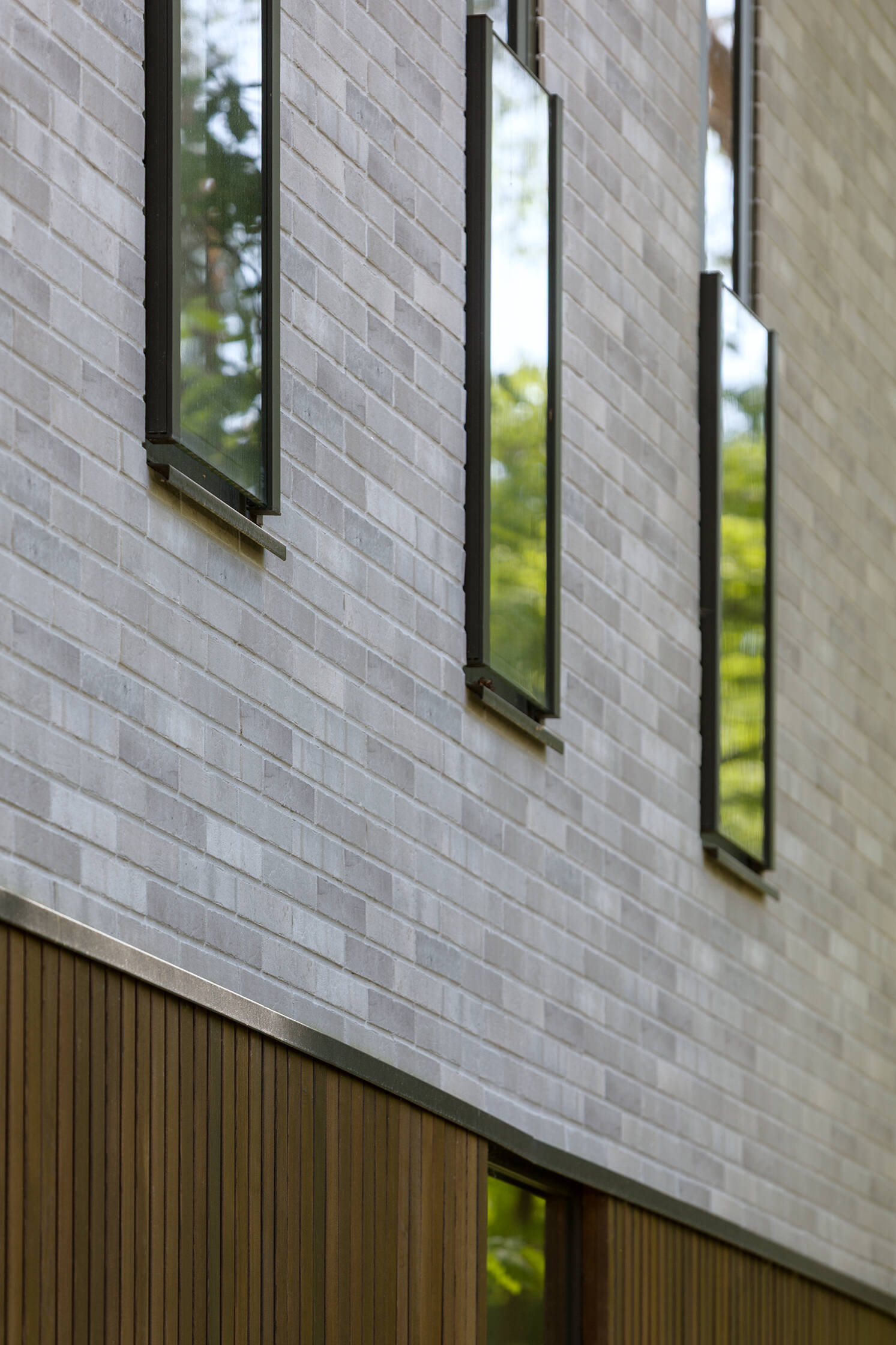 Expansive horizontal glazing and tall vertical windows bring daylight and views of the surrounding pine trees into The Intersecting House near Warsaw, with large living room glazing opening directly onto the terrace.