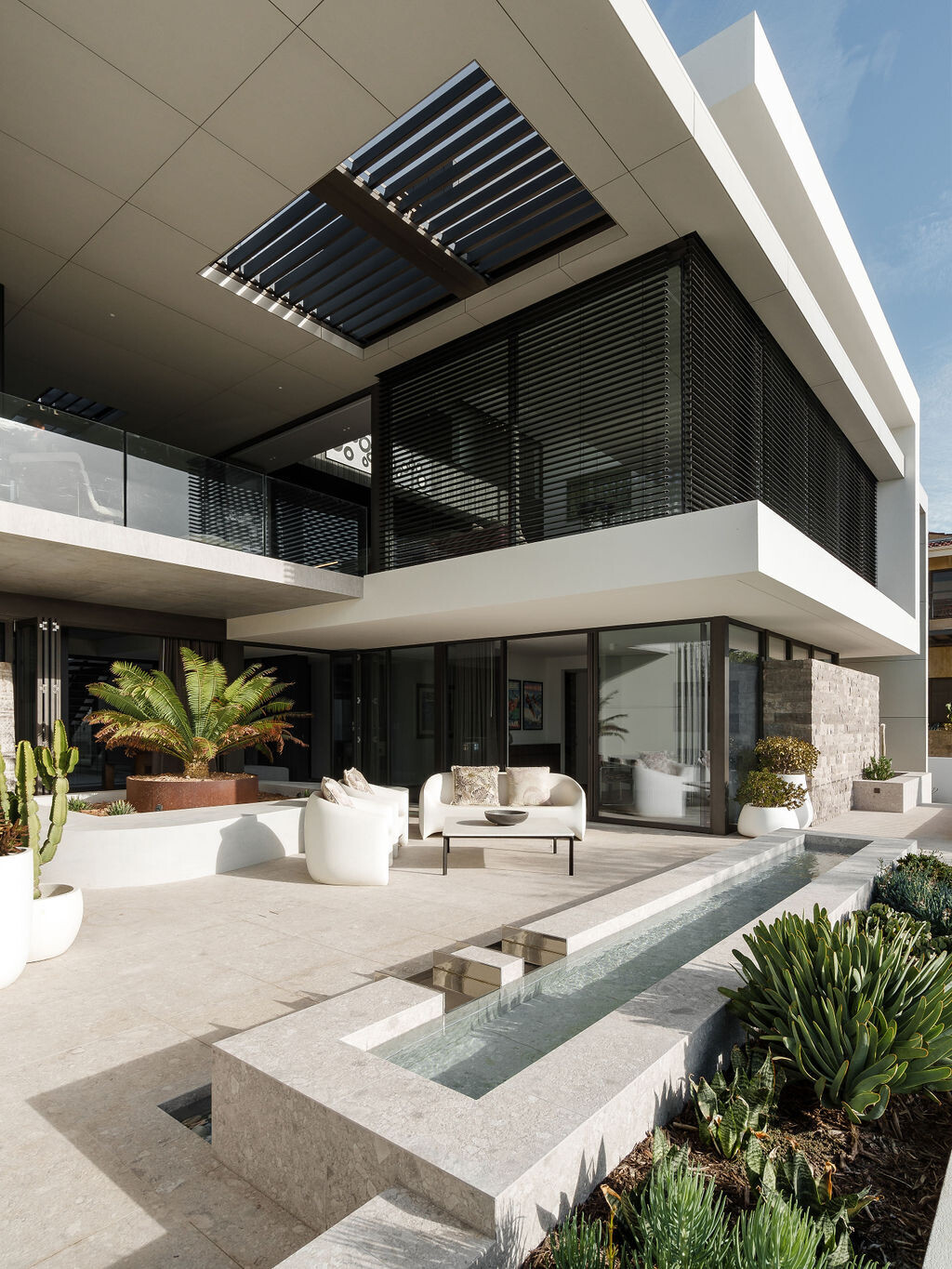 The front patio and water feature at Mezzanine House combine concrete, timber, landscaping and water in a contemporary Perth home designed by Craig Steere Architects.