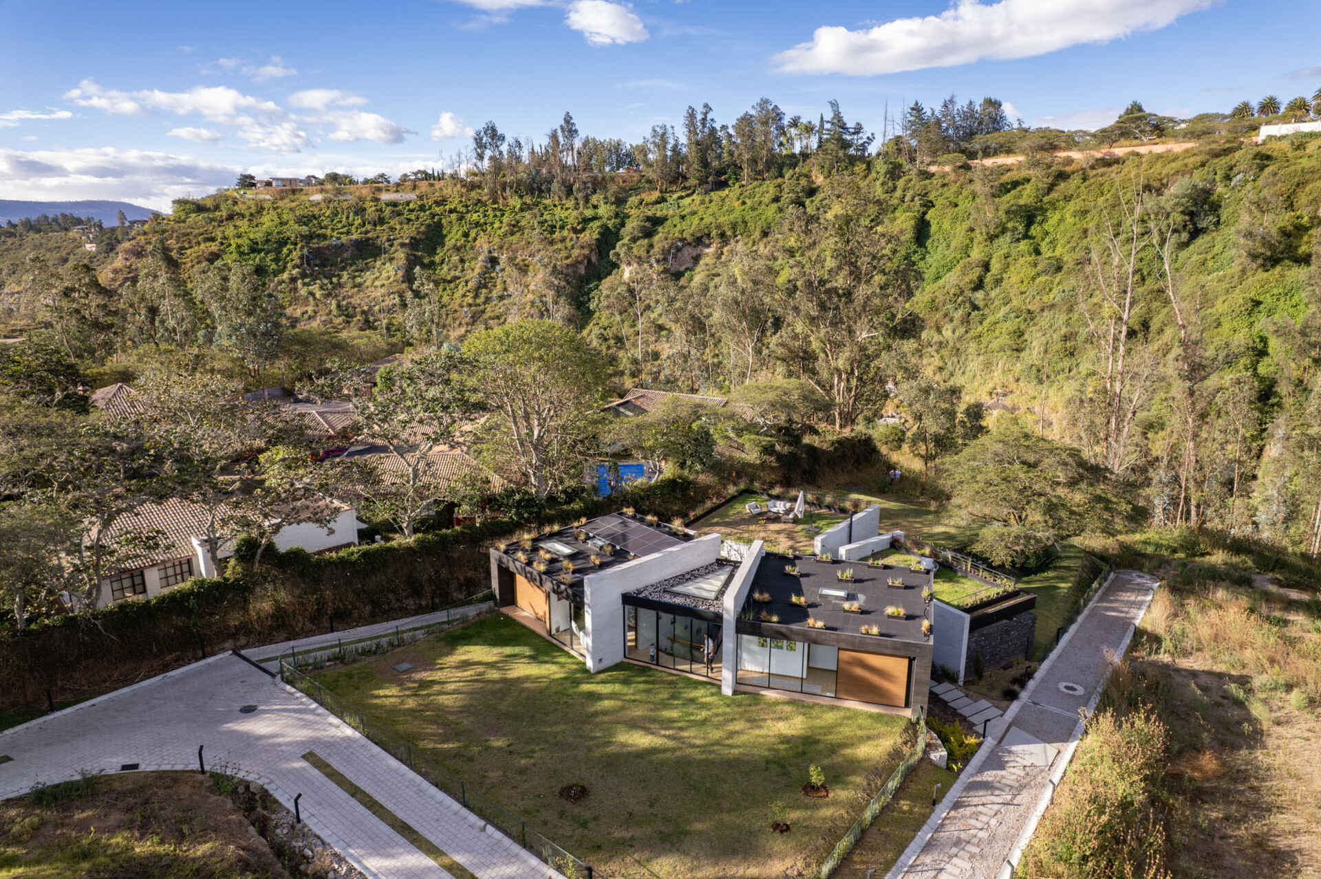 Explore a contemporary house in Puembo, Ecuador, with angular architecture, grass-covered roof terraces, a planted central courtyard, and sheltered outdoor living spaces. Designed by A1 Arquitectura Avanzada, the home combines pale walls, dark roof edges, wood-toned panels, and expansive glazing.