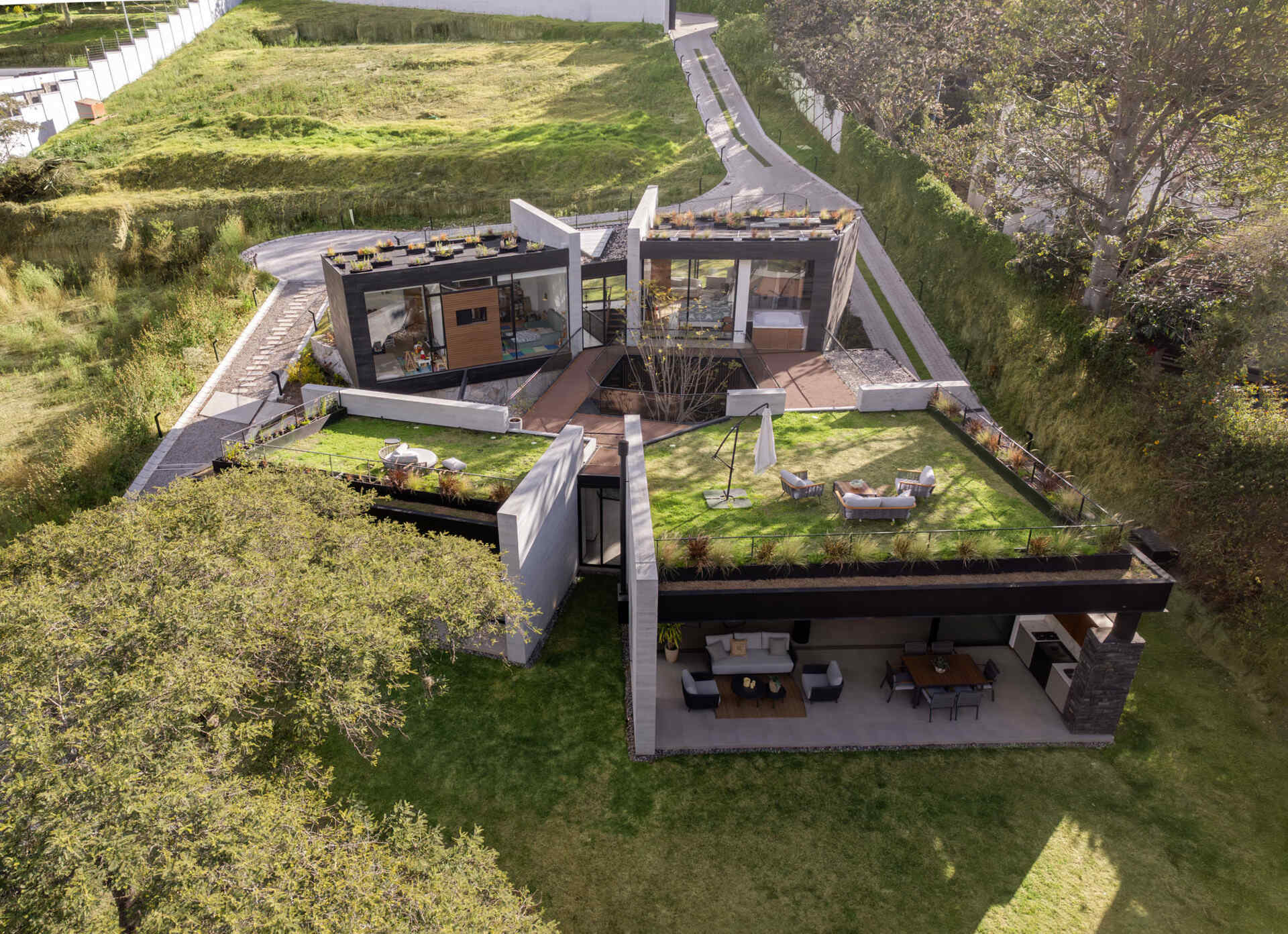 Explore a contemporary house in Puembo, Ecuador, with angular architecture, grass-covered roof terraces, a planted central courtyard, and sheltered outdoor living spaces. Designed by A1 Arquitectura Avanzada, the home combines pale walls, dark roof edges, wood-toned panels, and expansive glazing.