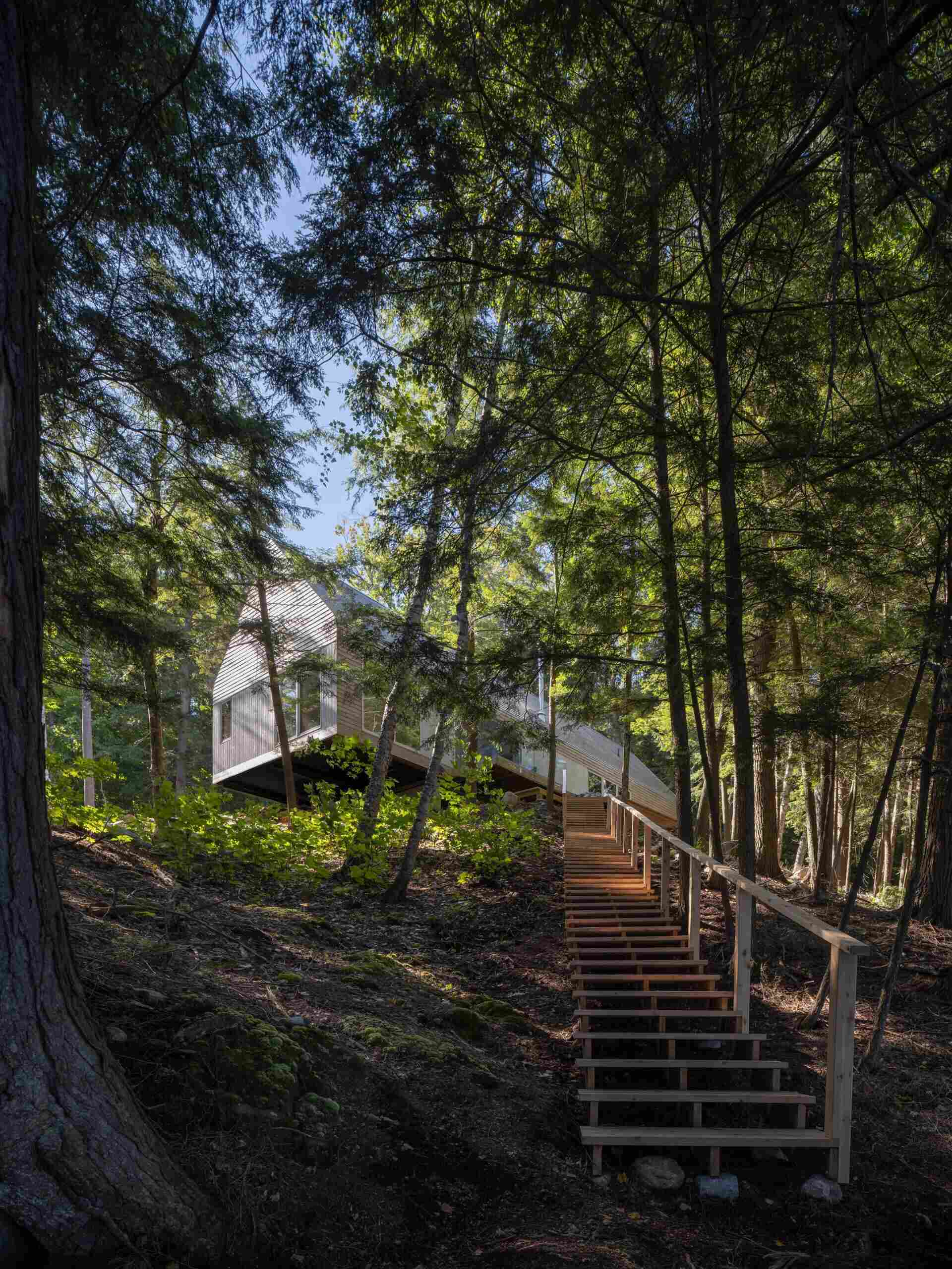 A modern prefab cottage in Magnetawan, Canada, designed with a simple gabled form, cedar siding, and an elevated structure that blends into the surrounding forest landscape.