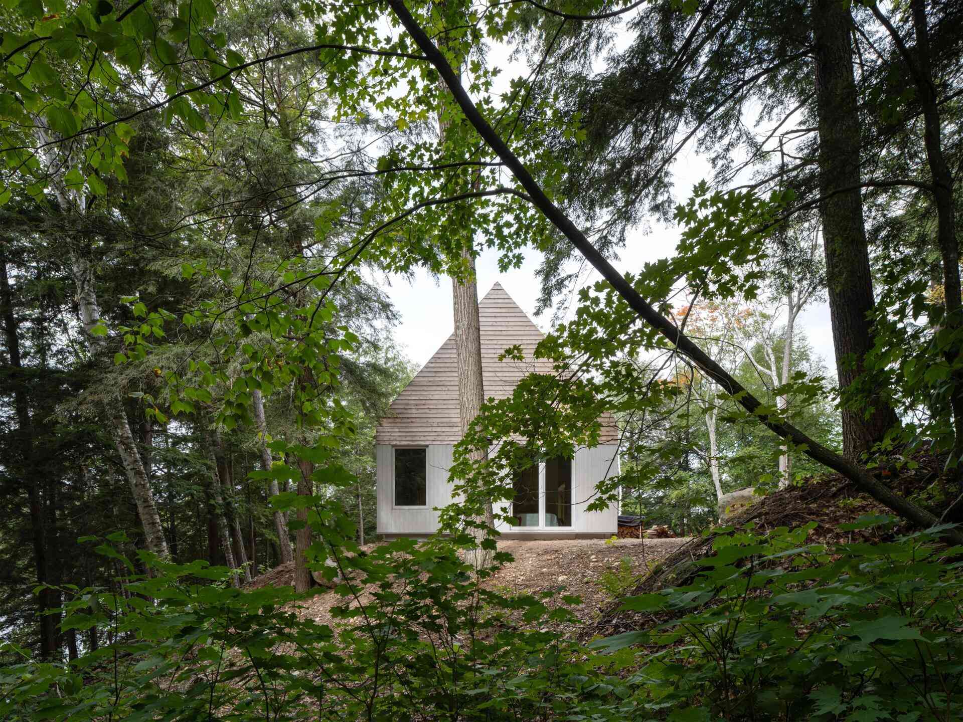 A modern prefab cottage in Magnetawan, Canada, designed with a simple gabled form, cedar siding, and an elevated structure that blends into the surrounding forest landscape.