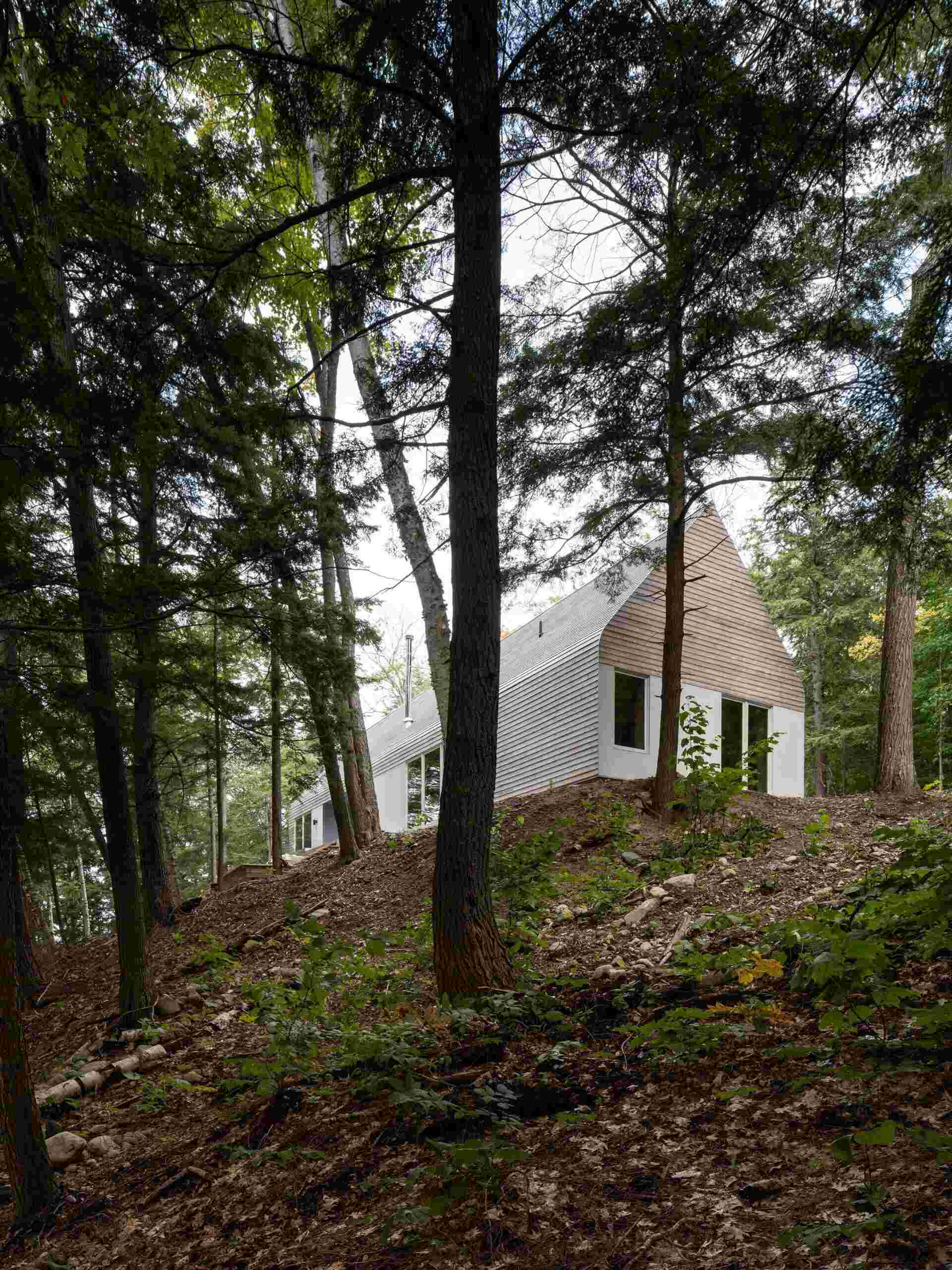A modern prefab cottage in Magnetawan, Canada, designed with a simple gabled form, cedar siding, and an elevated structure that blends into the surrounding forest landscape.