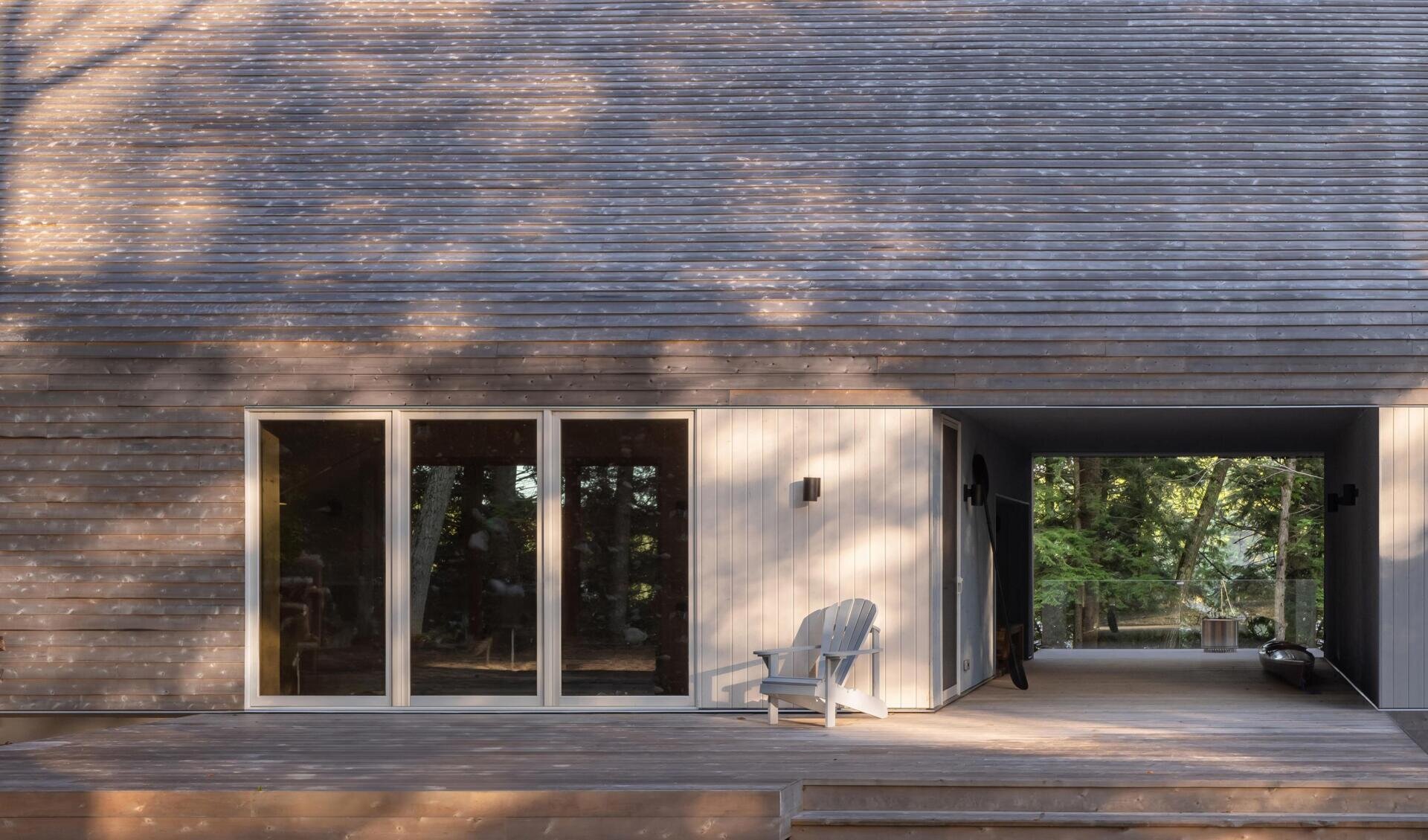 The breezeway at this Ontario cottage creates a sheltered outdoor living space with timber finishes, lake views, a kayak storage area, and a seamless connection between indoor and outdoor living.