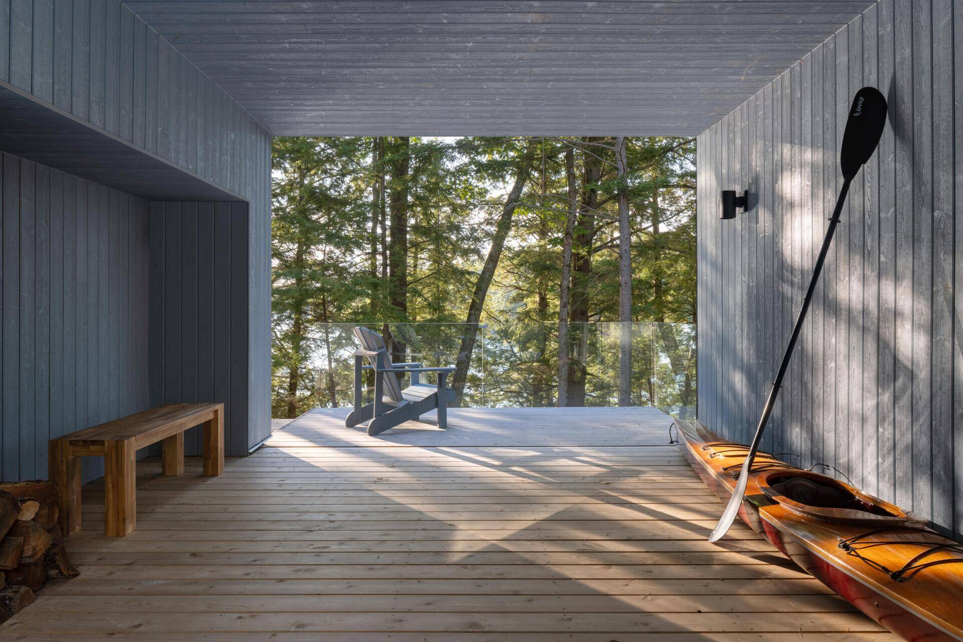 The breezeway at this Ontario cottage creates a sheltered outdoor living space with timber finishes, lake views, a kayak storage area, and a seamless connection between indoor and outdoor living.