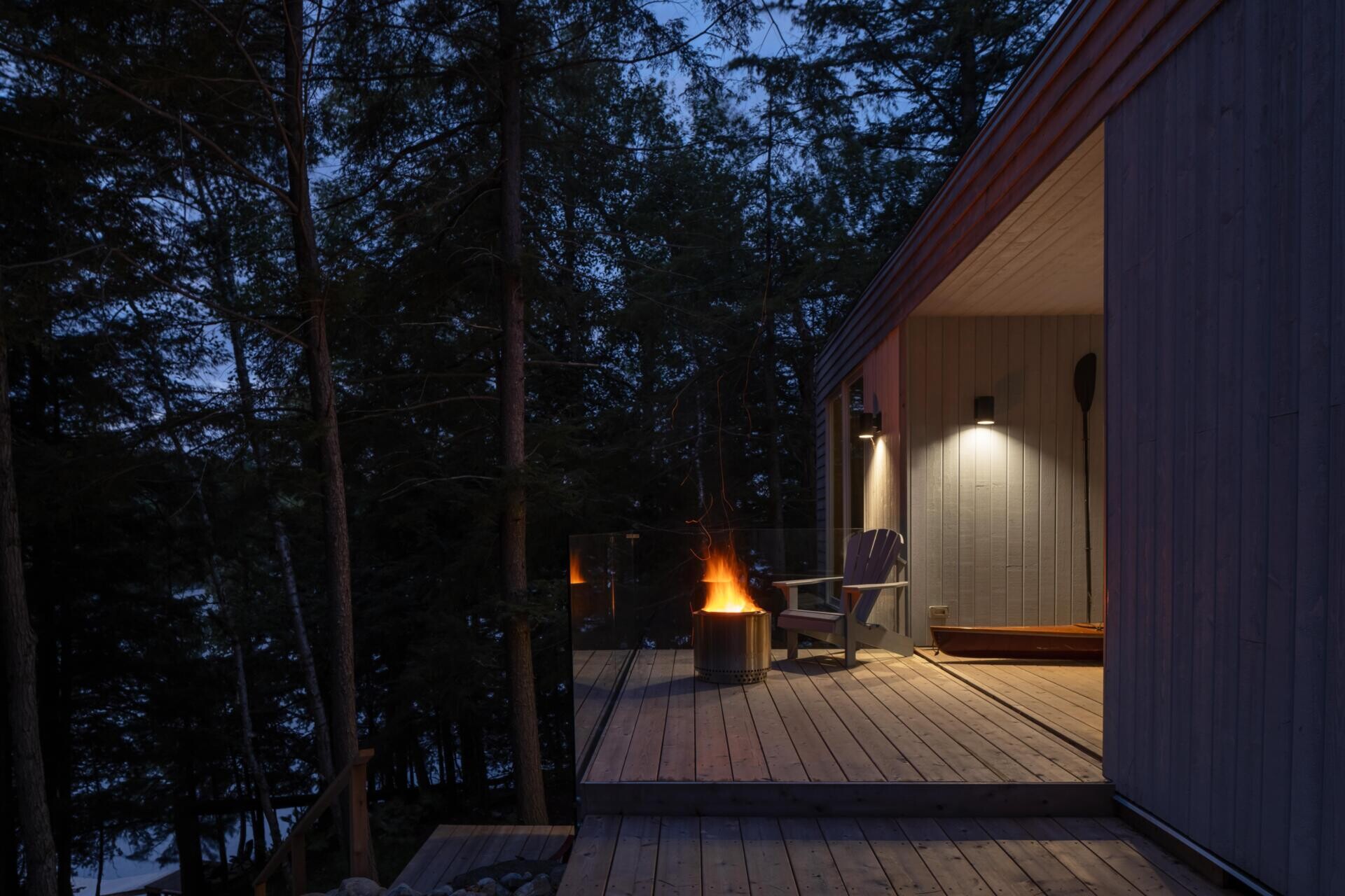 The breezeway at this Ontario cottage creates a sheltered outdoor living space with timber finishes, lake views, a kayak storage area, and a seamless connection between indoor and outdoor living.