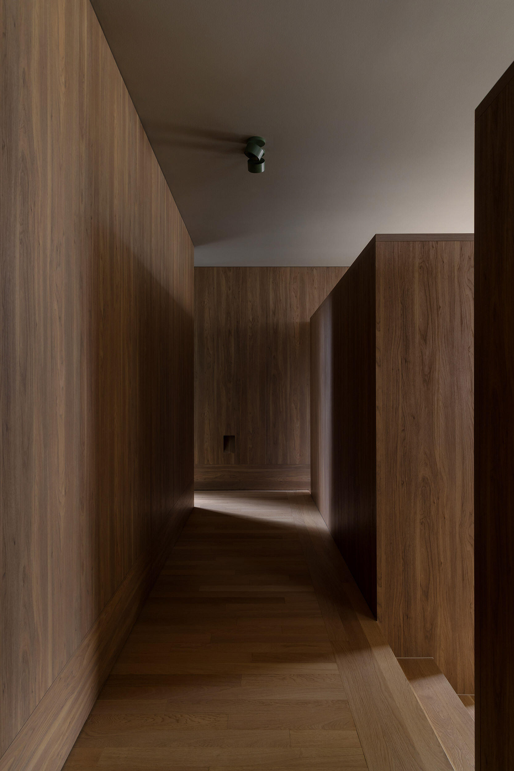 This wood-lined hallway provides access to a combined TV room and library, a laundry room, and a powder-room. From there, steps lead down to the kitchen and dining room, where the house begins to open up.
