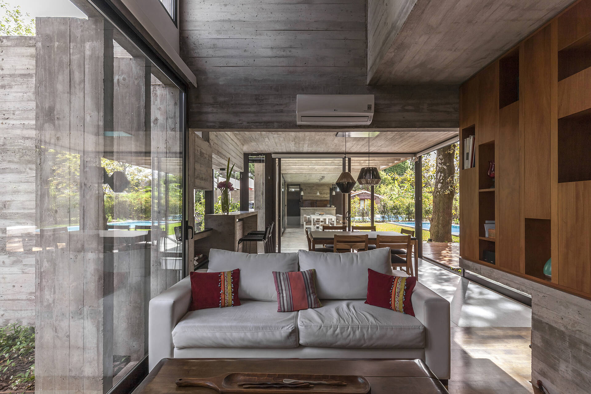 Explore the modern living room of Casa Aranzazu, where exposed concrete, warm wood shelving, large windows and a built-in fireplace create a clean yet inviting interior.