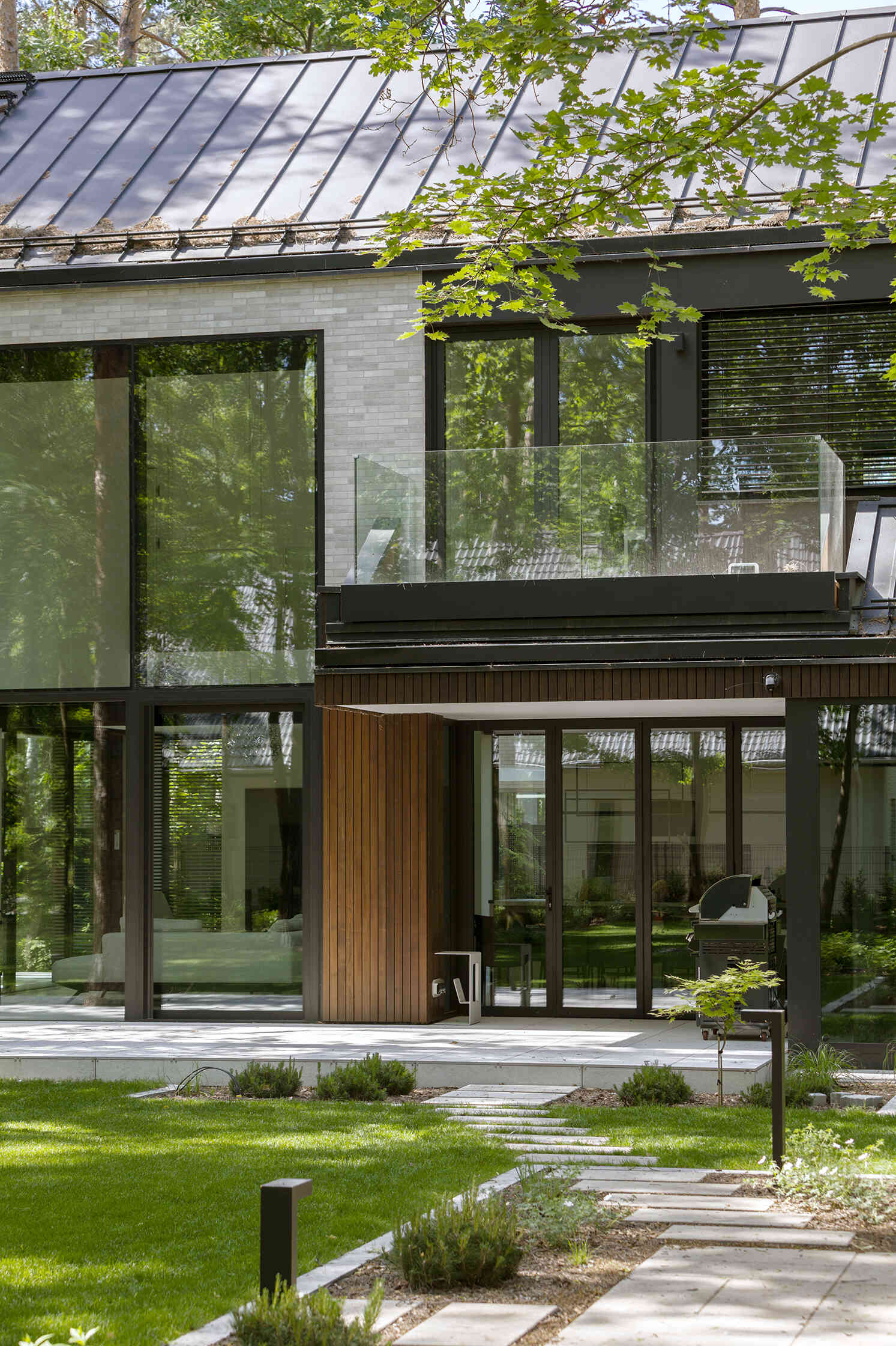 The covered west-facing terrace at The Intersecting House creates a sheltered outdoor space beneath the upper volume. Large openings connect the terrace with the double-height living room and garden.