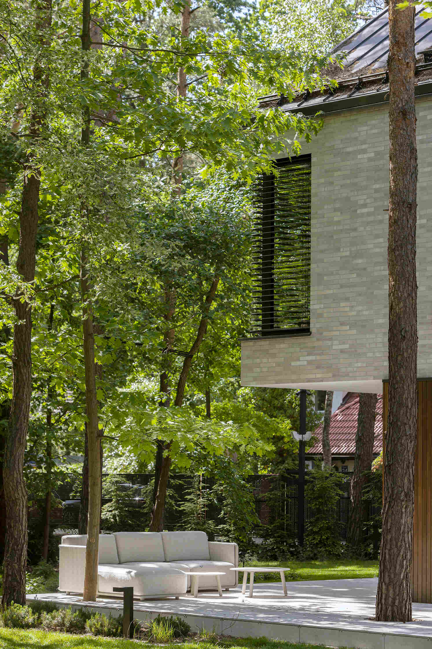 The covered west-facing terrace at The Intersecting House creates a sheltered outdoor space beneath the upper volume. Large openings connect the terrace with the double-height living room and garden.