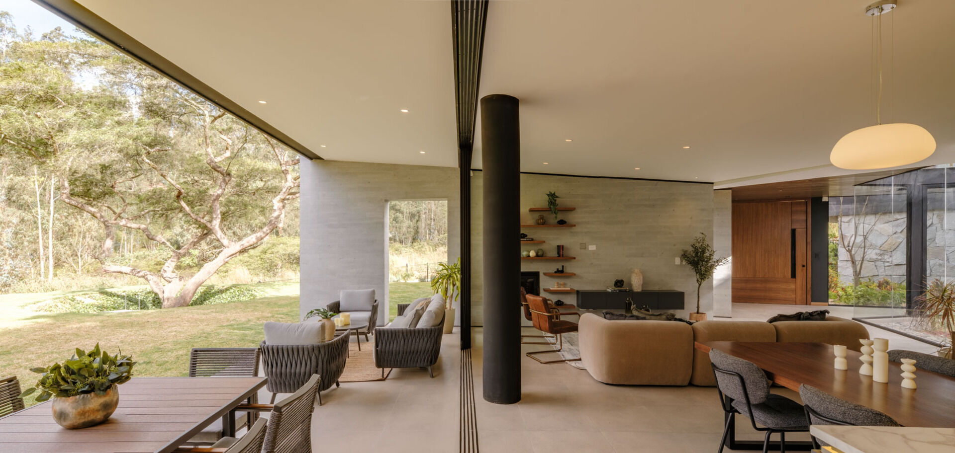 A covered patio opens directly from the living and dining rooms through wide sliding glass doors. Woven outdoor seating, a dining table, and a built-in grill and sink create a sheltered space overlooking the lawn at this contemporary home in Ecuador.