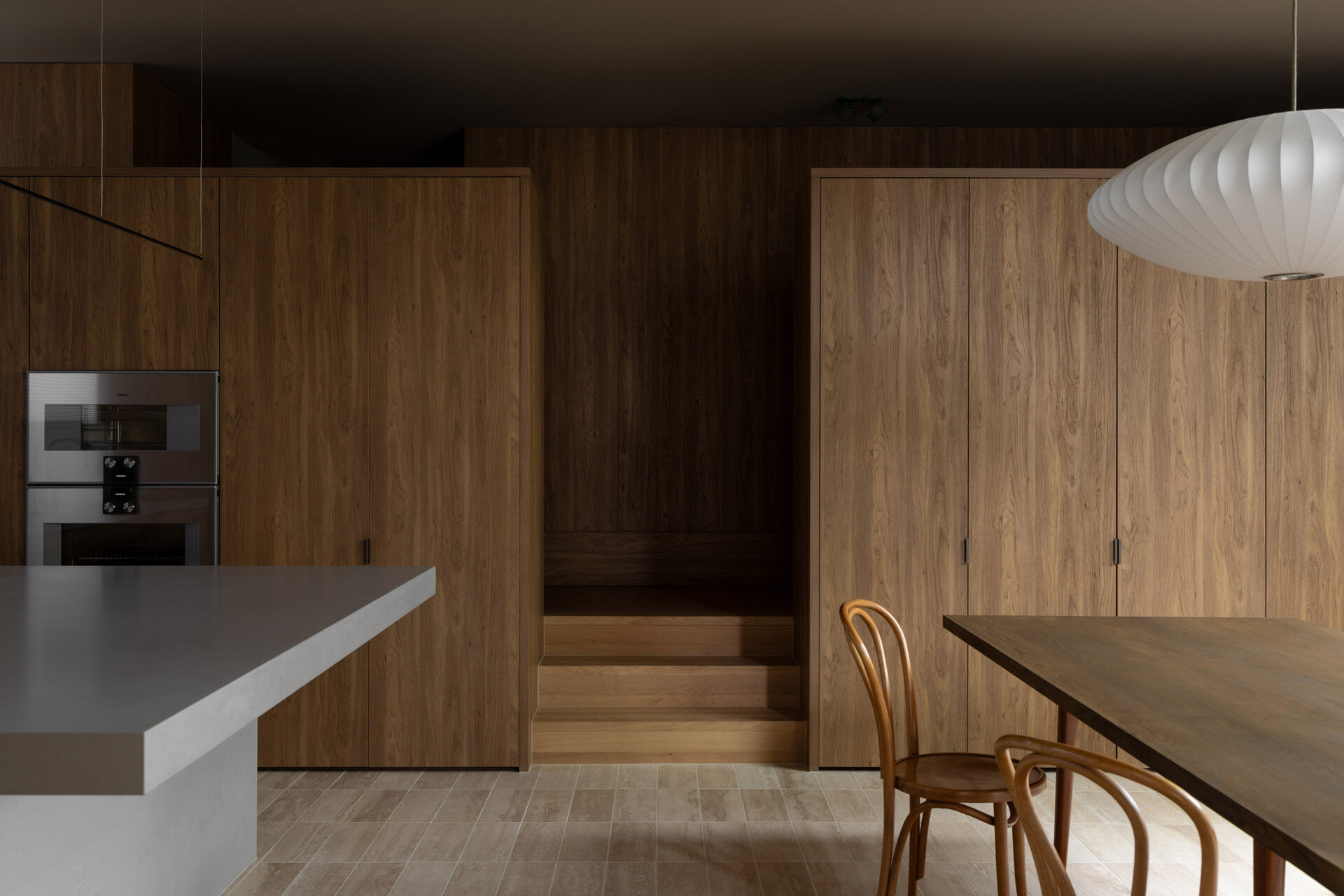 This wood-lined hallway provides access to a combined TV room and library, a laundry room, and a powder-room. From there, steps lead down to the kitchen and dining room, where the house begins to open up.