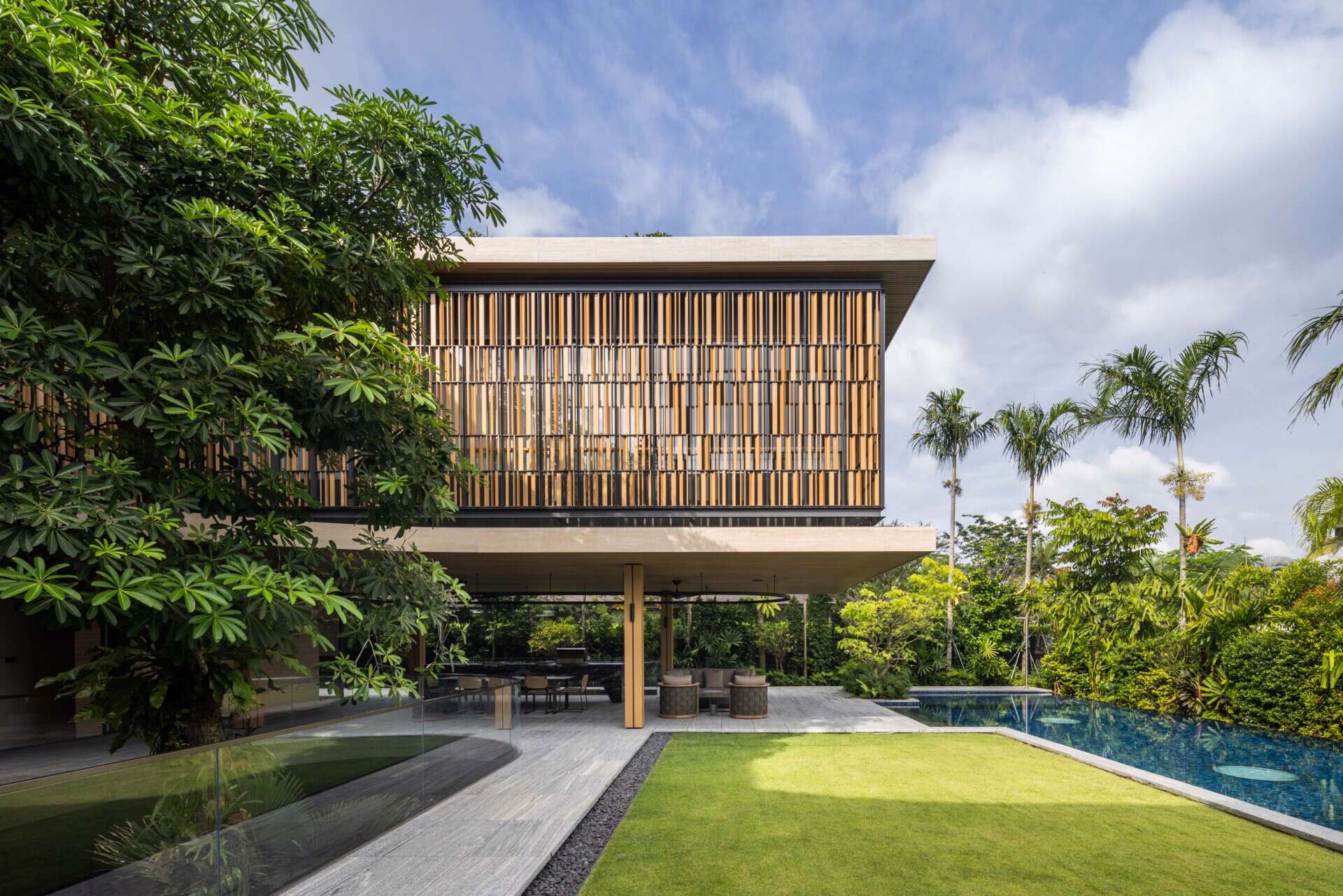 A modern house open to the outdoors with a covered outdoor living room and swimming pool.
