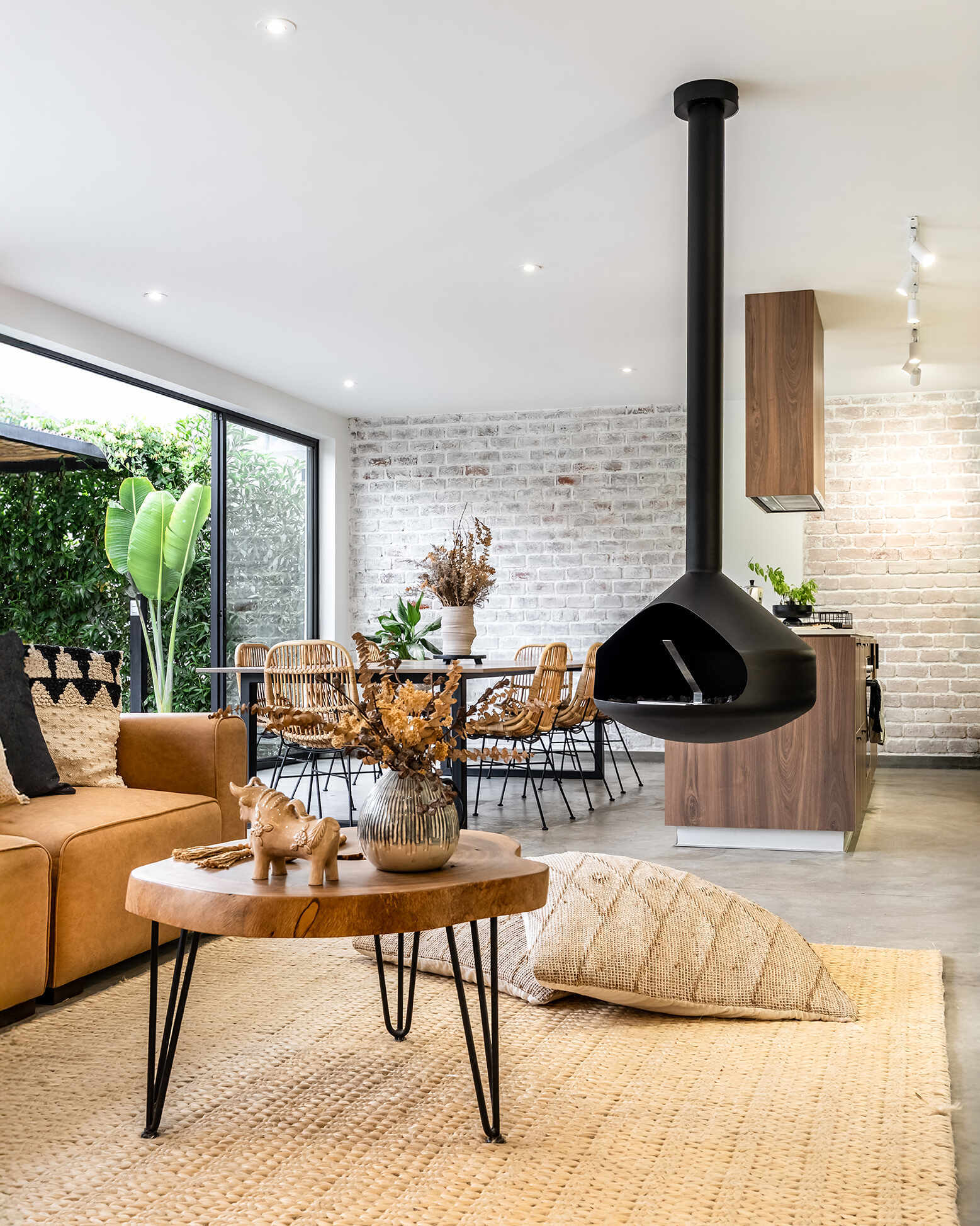 Casa Berna’s living room pairs a suspended black fireplace with a tan sofa, woven rug and timber table, beside sliding doors that look onto the garden.