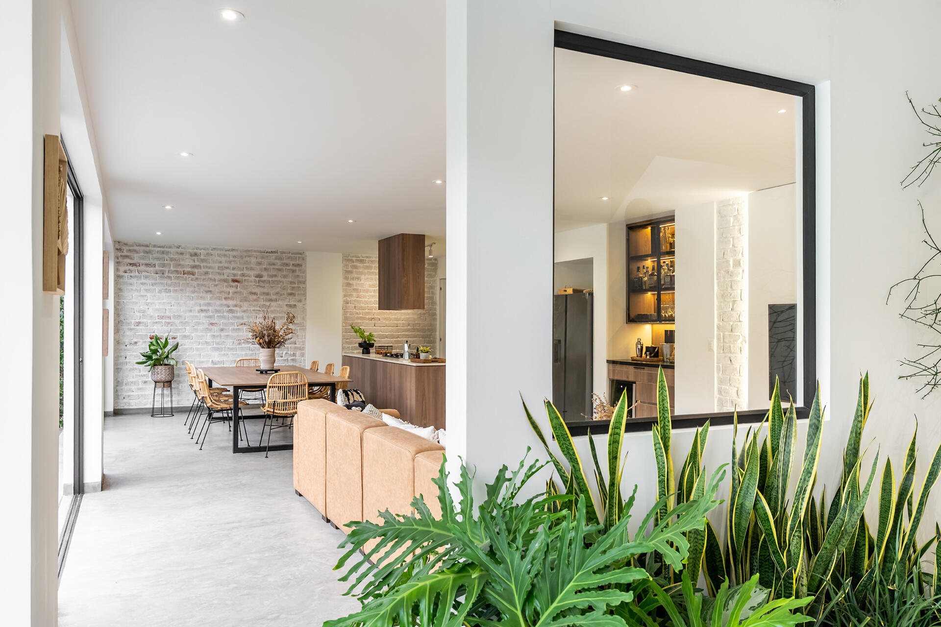 A large internal window and indoor planting mark the entry to Casa Berna, with views through to the kitchen, bar, living area, dining table and kitchen.