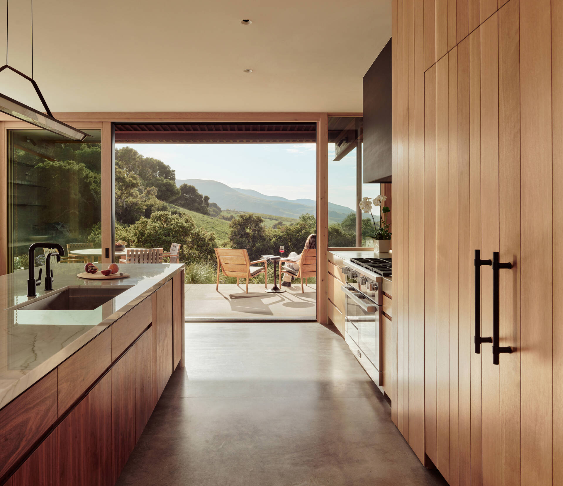 See how natural materials including white oak, walnut, slab stone and blackened steel come together in the central kitchen of Clayton Korte’s Vineyard Residence.