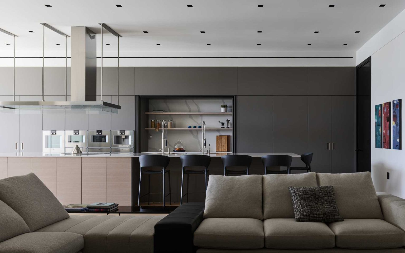 Grey cabinetry stretches along the kitchen and dining wall of Nanton House, contrasting with warm wood floors and millwork, while an island provides bar seating and garden views.