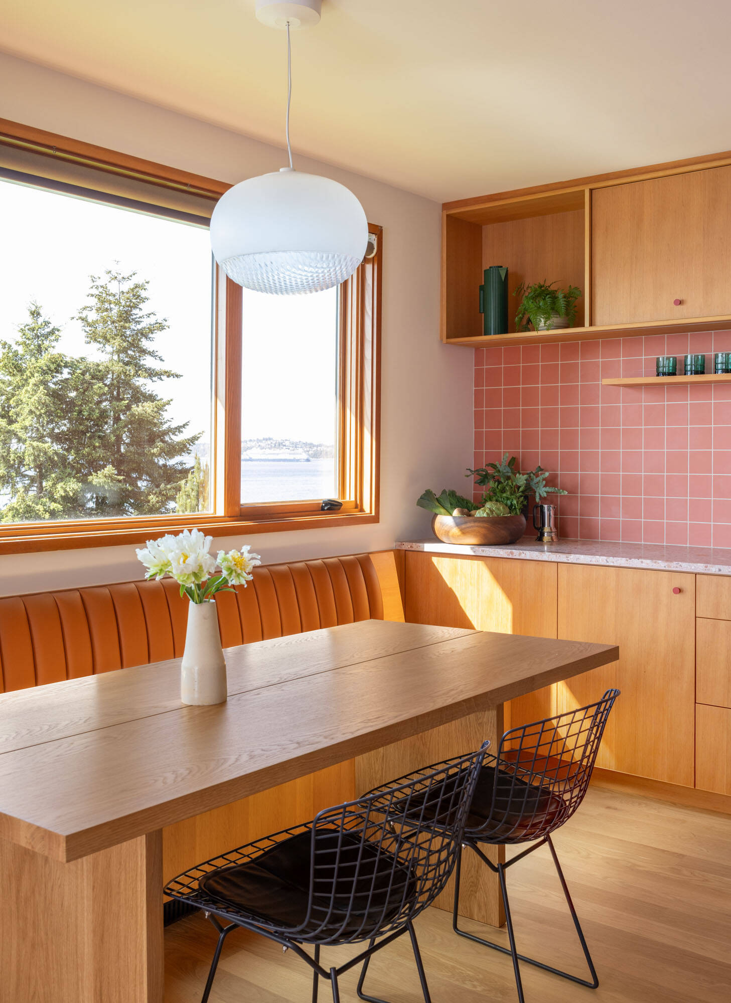 Tour the remodeled kitchen and dining area, where SHED flipped the original layout so a built-in banquette now faces Puget Sound, paired with warm timber cabinetry, pink Concrete Collaborative counters and a Zia Tile backsplash.