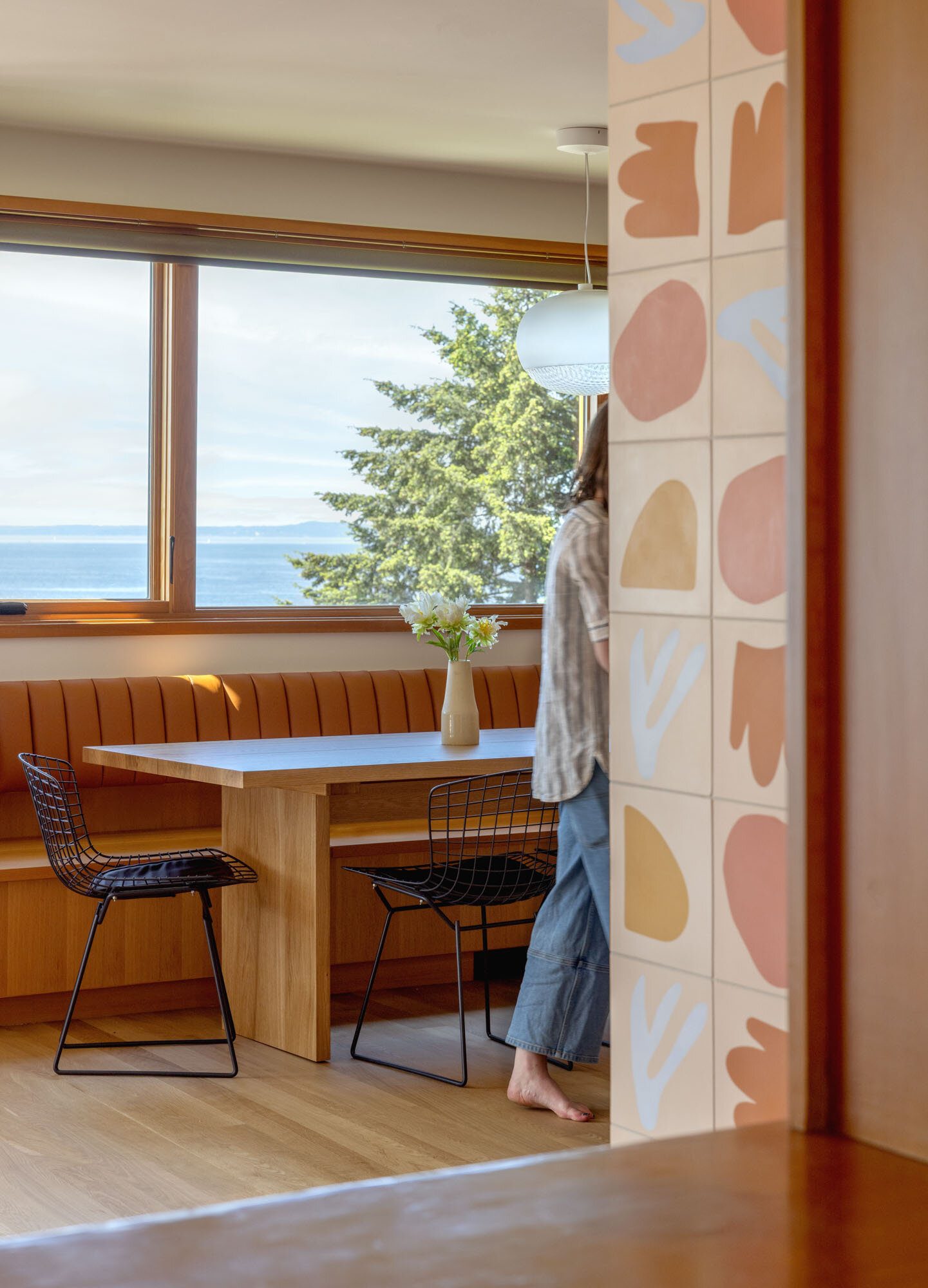Tour the remodeled kitchen and dining area, where SHED flipped the original layout so a built-in banquette now faces Puget Sound, paired with warm timber cabinetry, pink Concrete Collaborative counters and a Zia Tile backsplash.