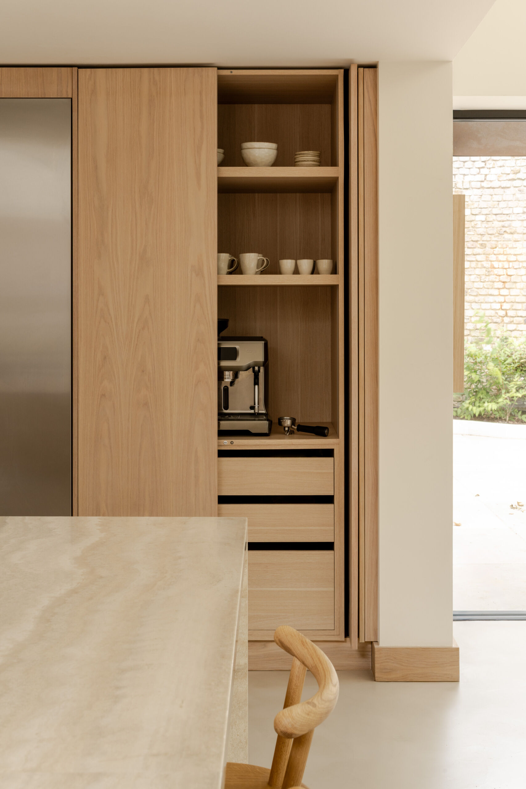 Discover the spacious kitchen at Thirsk Cottage, with pale wood cabinetry, a travertine island, microcement flooring and skylights beneath the dramatic vaulted roof.