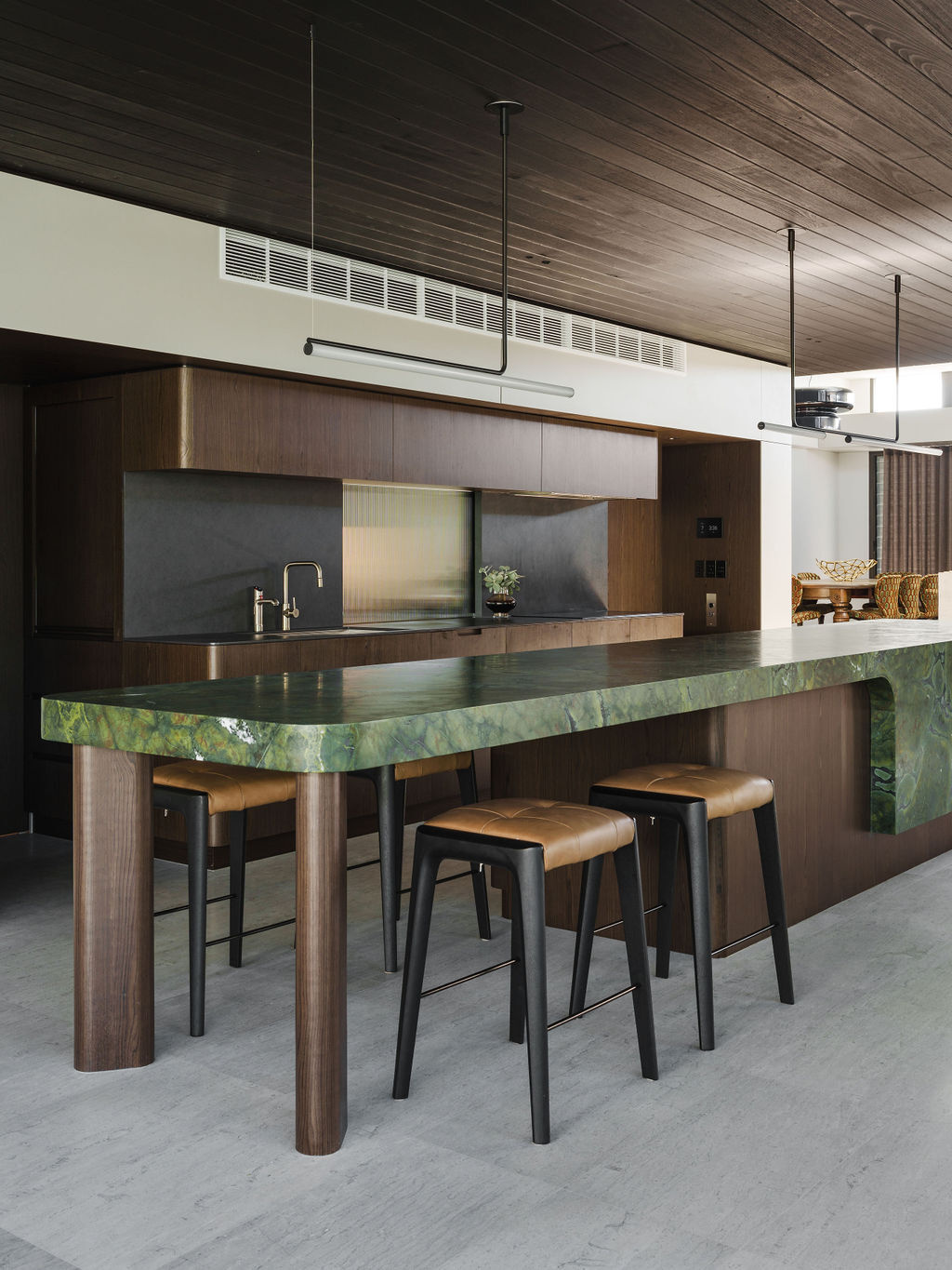 The kitchen at Mezzanine House combines rich timber cabinetry, a dramatic green stone island, dark timber ceilings and an open connection to the living area.
