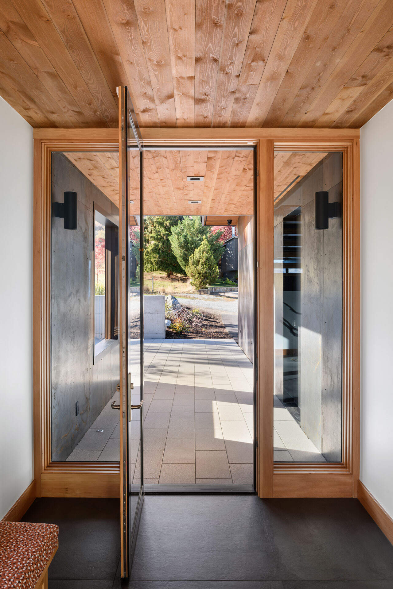 A bright modern entryway combines warm timber, charcoal floor tiles, a built-in bench, and an open-riser staircase with black steel details.