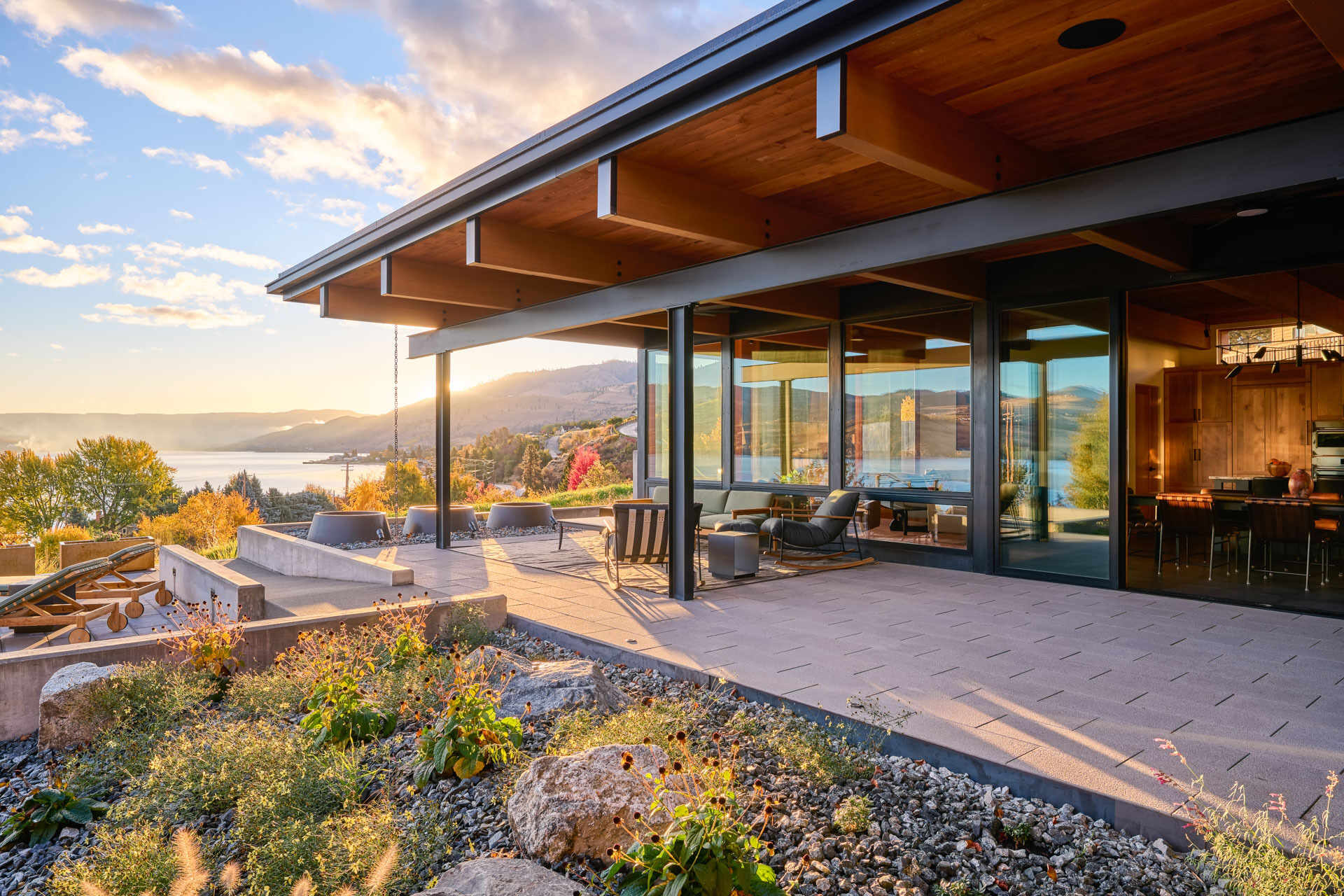 A repurposed shipping container pool anchors an outdoor living space, surrounded by a protected courtyard, covered patio, and views across the landscape.