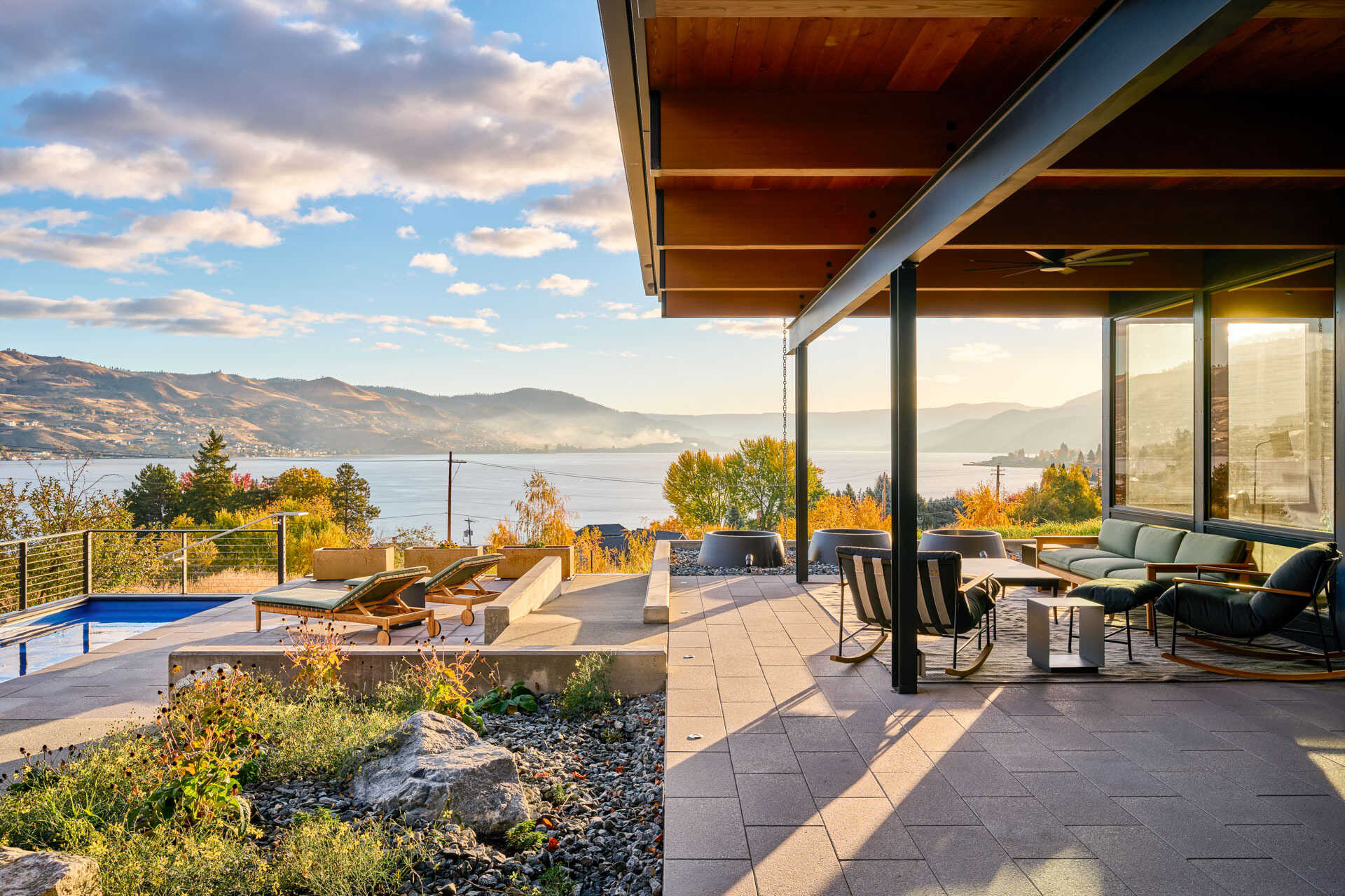 A repurposed shipping container pool anchors an outdoor living space, surrounded by a protected courtyard, covered patio, and views across the landscape.