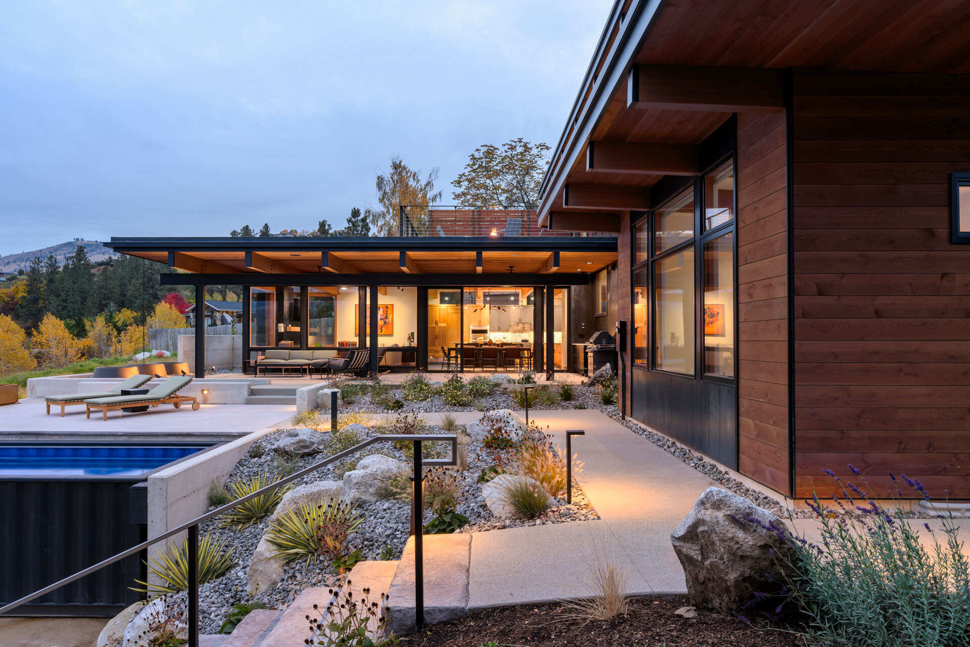A repurposed shipping container pool anchors an outdoor living space, surrounded by a protected courtyard, covered patio, and views across the landscape.
