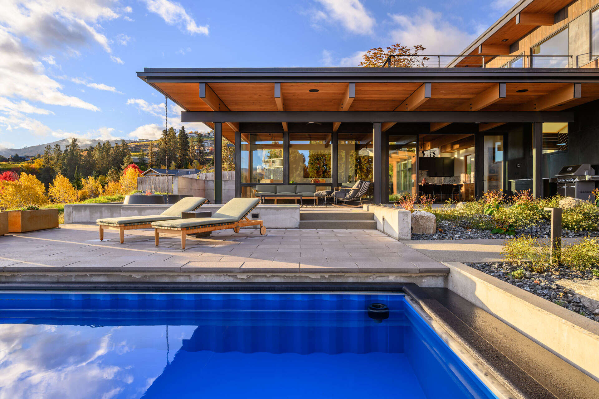 A repurposed shipping container pool anchors an outdoor living space, surrounded by a protected courtyard, covered patio, and views across the landscape.