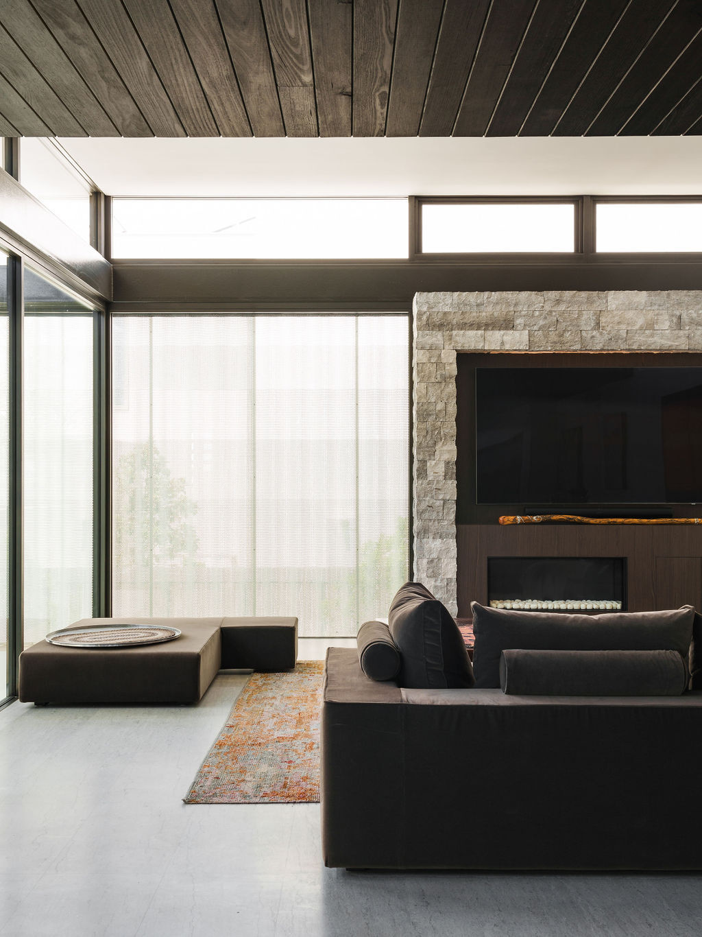 The main living room at Mezzanine House features a fireplace and television area within an open-plan space designed around family living and outdoor connections.