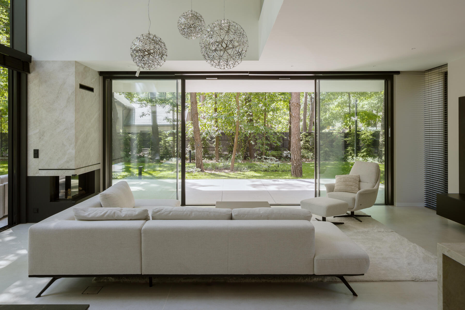 The double-height living room at The Intersecting House connects both levels of the home while opening toward the garden through expansive glazing. The space brings together daylight, forest views and direct terrace access.