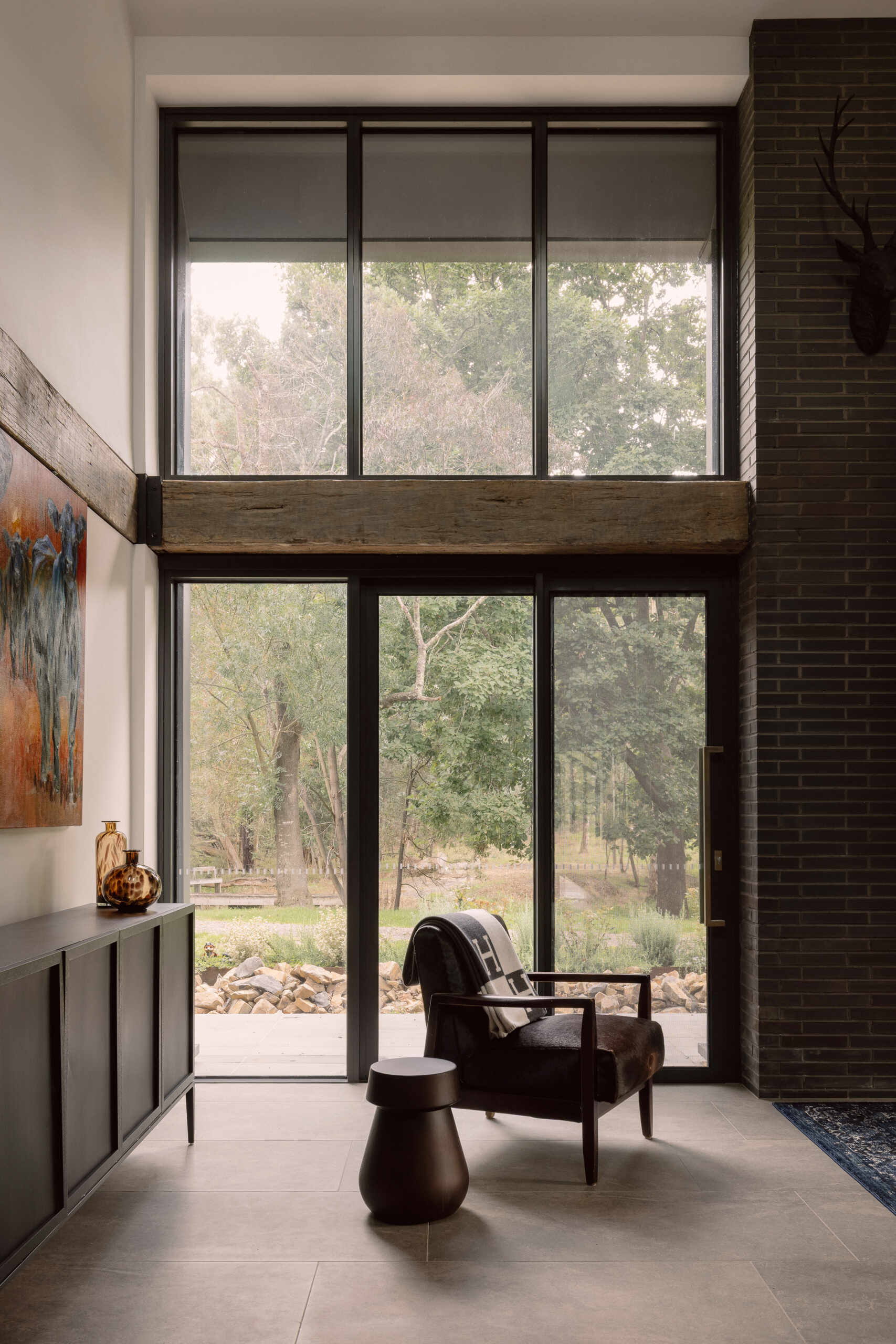 Step inside the living room of Yarra Valley House, featuring a large sectional, dark brick, exposed timber beams, grey flooring and expansive views.