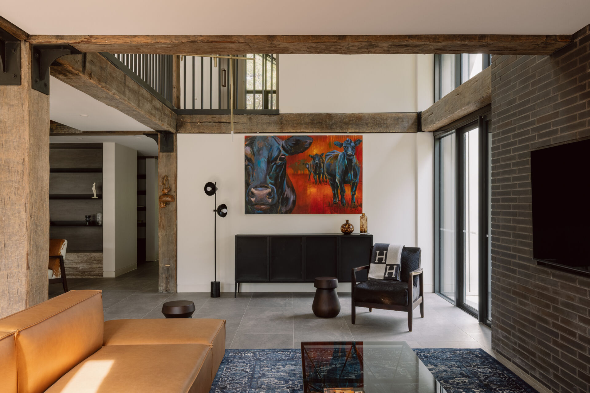 Step inside the living room of Yarra Valley House, featuring a large sectional, dark brick, exposed timber beams, grey flooring and expansive views.