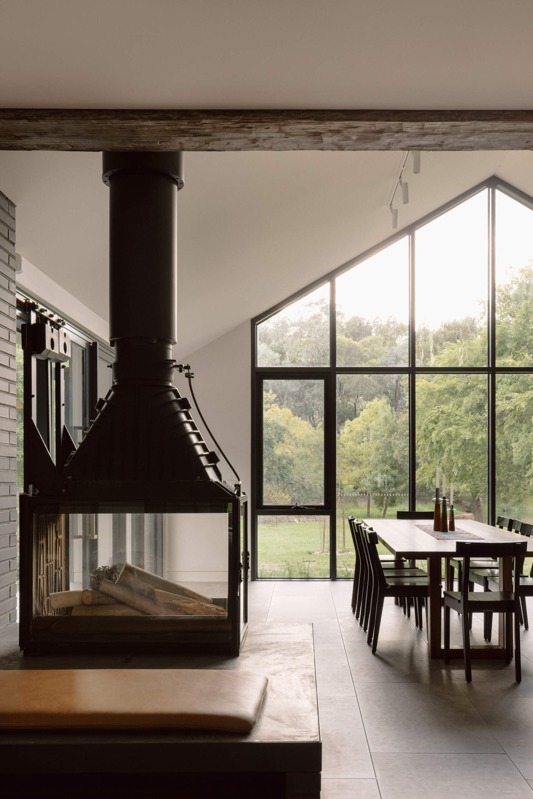 See the dramatic fireplace and reclaimed timber beams inside Yarra Valley House, where dark masonry and natural timber create a warm contemporary living space.