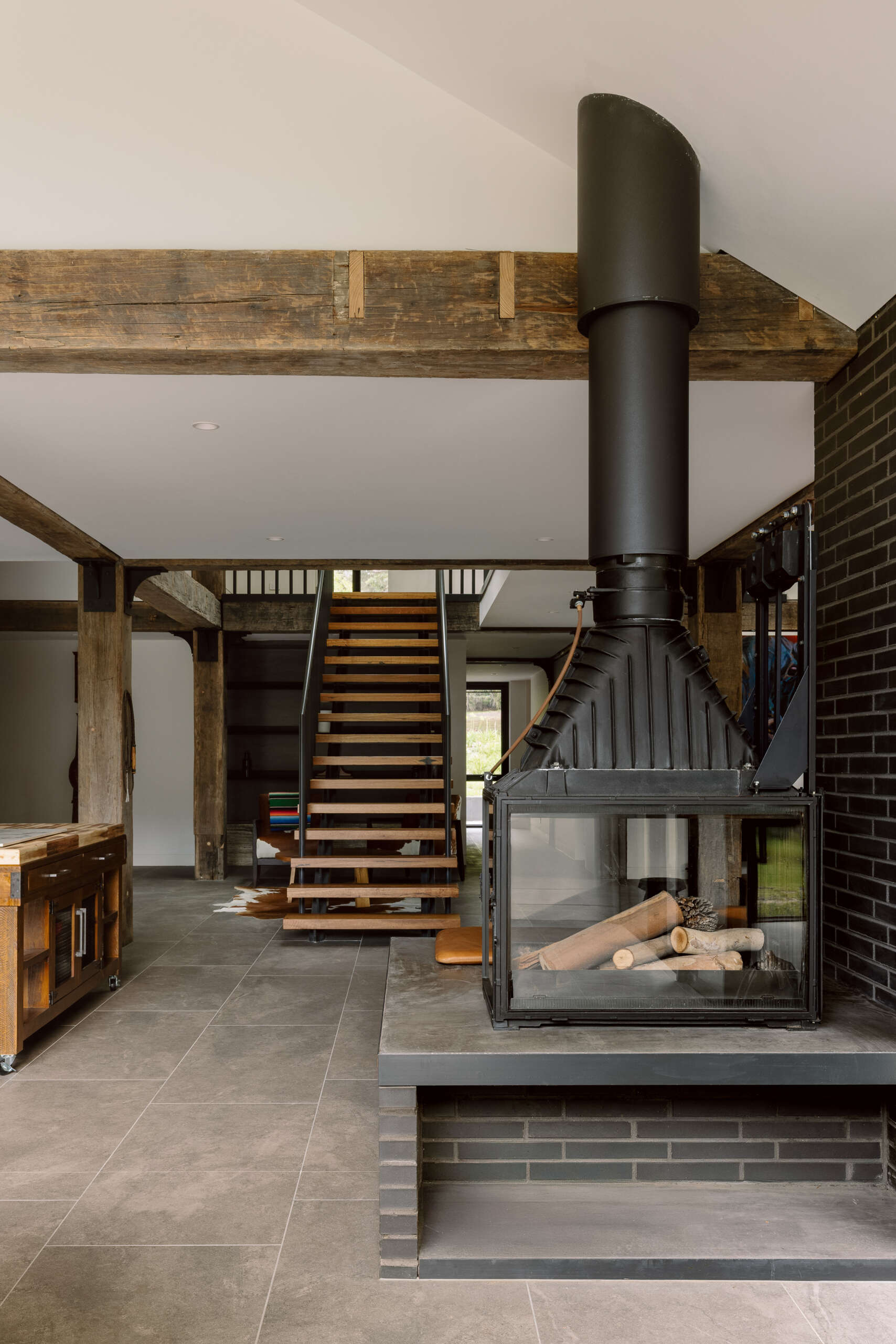See the dramatic fireplace and reclaimed timber beams inside Yarra Valley House, where dark masonry and natural timber create a warm contemporary living space.