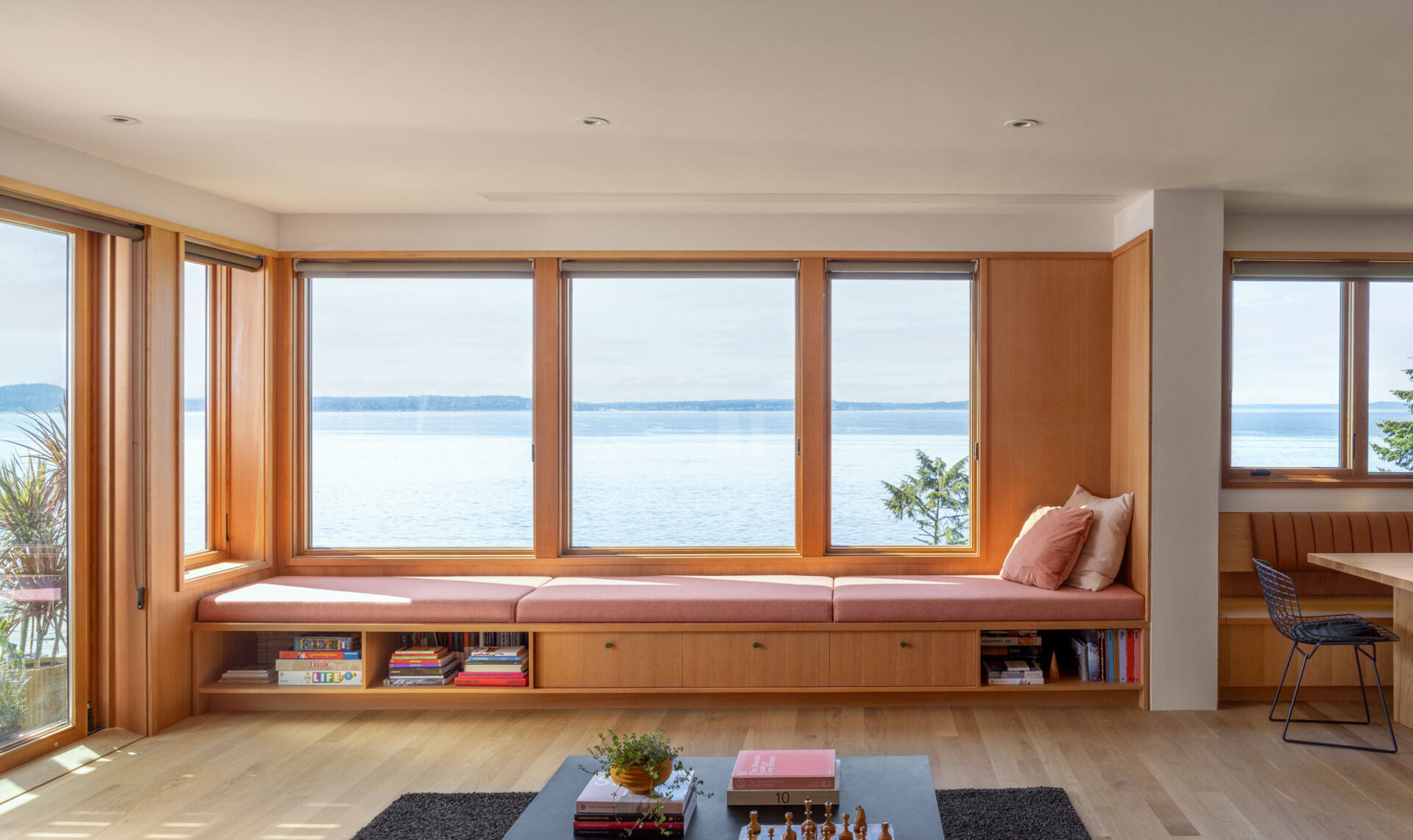 Step inside the renovated living room at Alki Lookout, where pale timber, pink upholstery, patterned tile and a long built-in window bench create a warm place to sit and watch ferries cross Puget Sound.