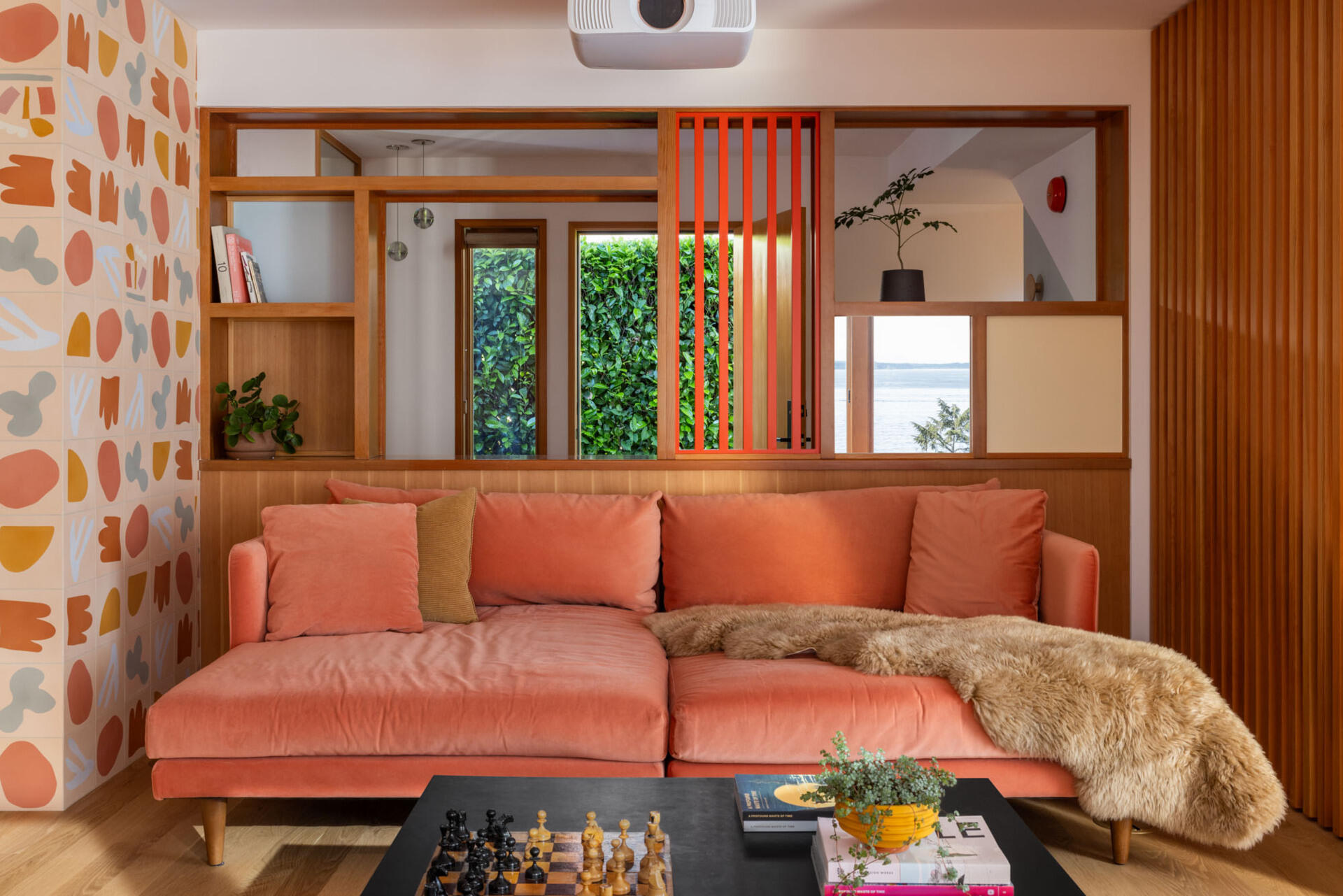 Step inside the renovated living room at Alki Lookout, where pale timber, pink upholstery, patterned tile and a long built-in window bench create a warm place to sit and watch ferries cross Puget Sound.