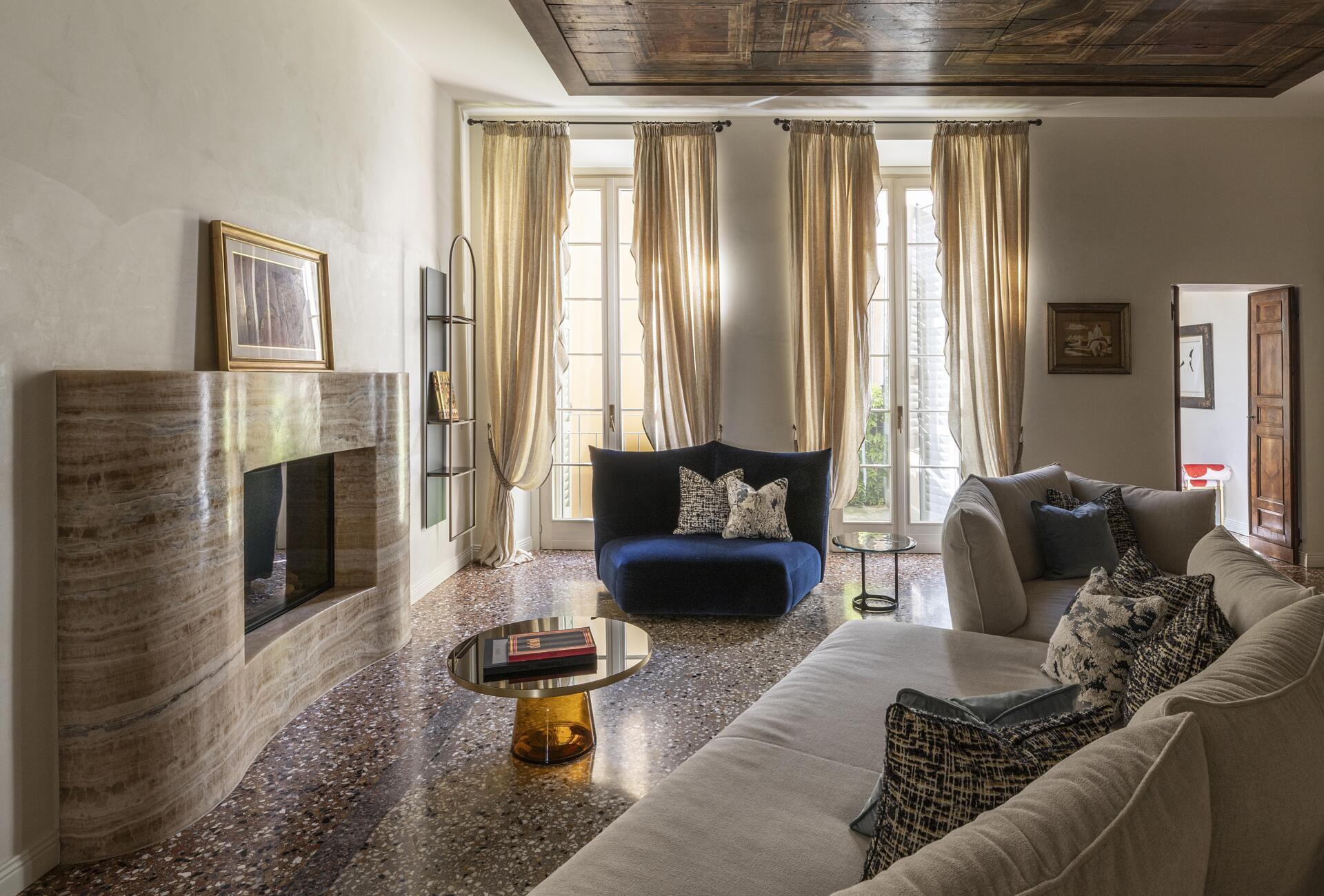 A sculptural onyx fireplace becomes the centrepiece of this Italian palazzo living room, paired with a large double-sided sofa, brass details and Venetian terrazzo.