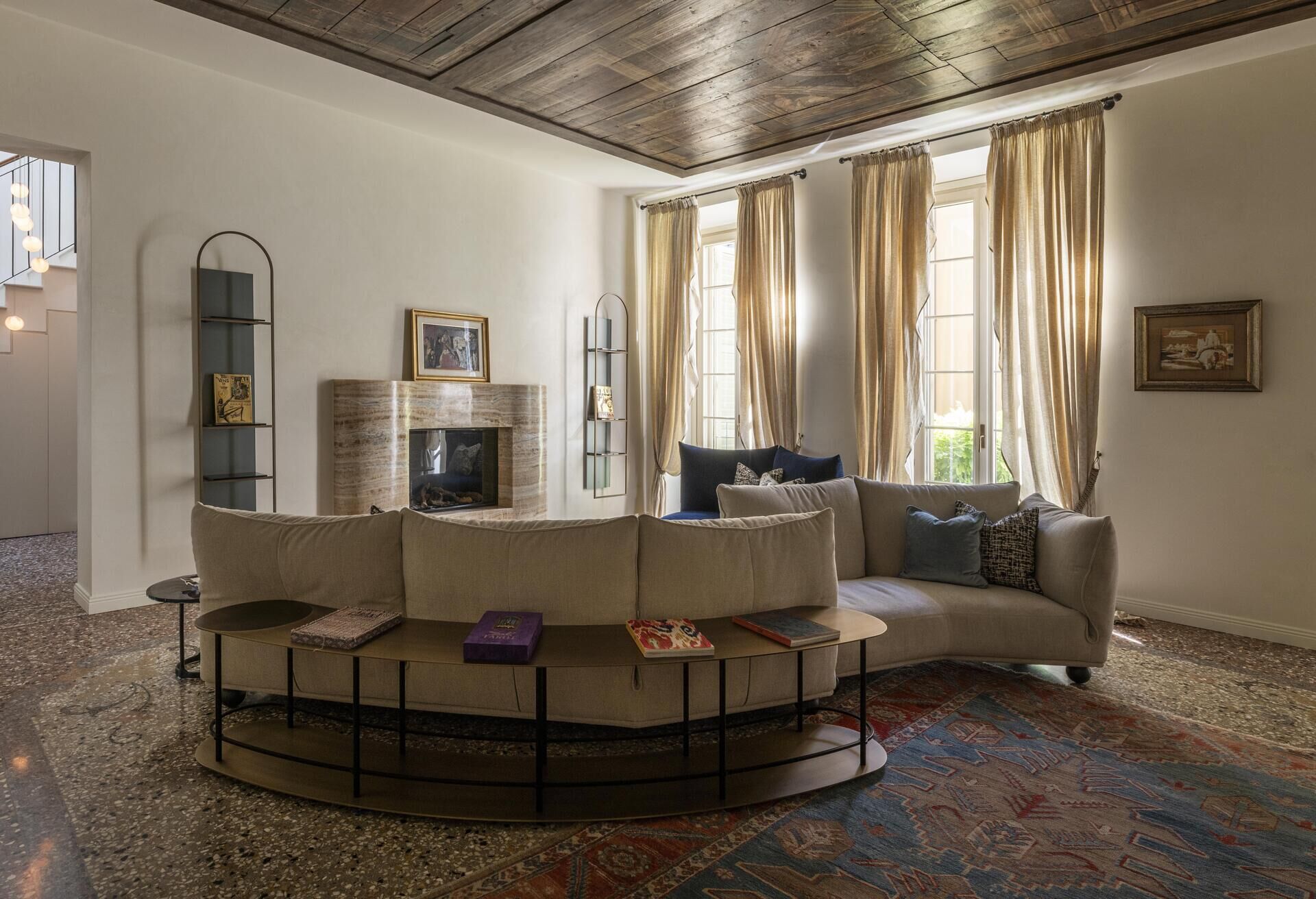 A sculptural onyx fireplace becomes the centrepiece of this Italian palazzo living room, paired with a large double-sided sofa, brass details and Venetian terrazzo.