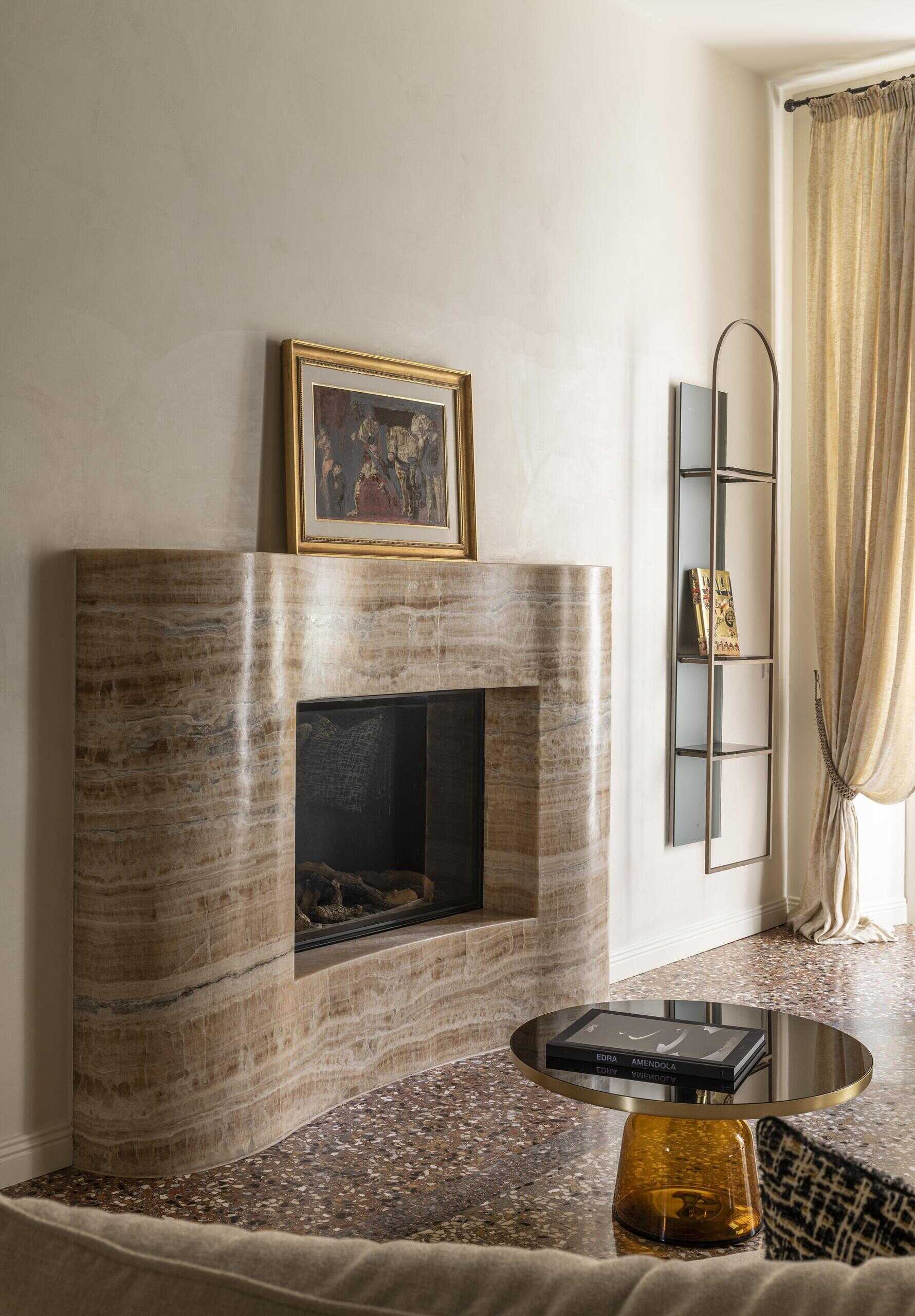 A sculptural onyx fireplace becomes the centrepiece of this Italian palazzo living room, paired with a large double-sided sofa, brass details and Venetian terrazzo.