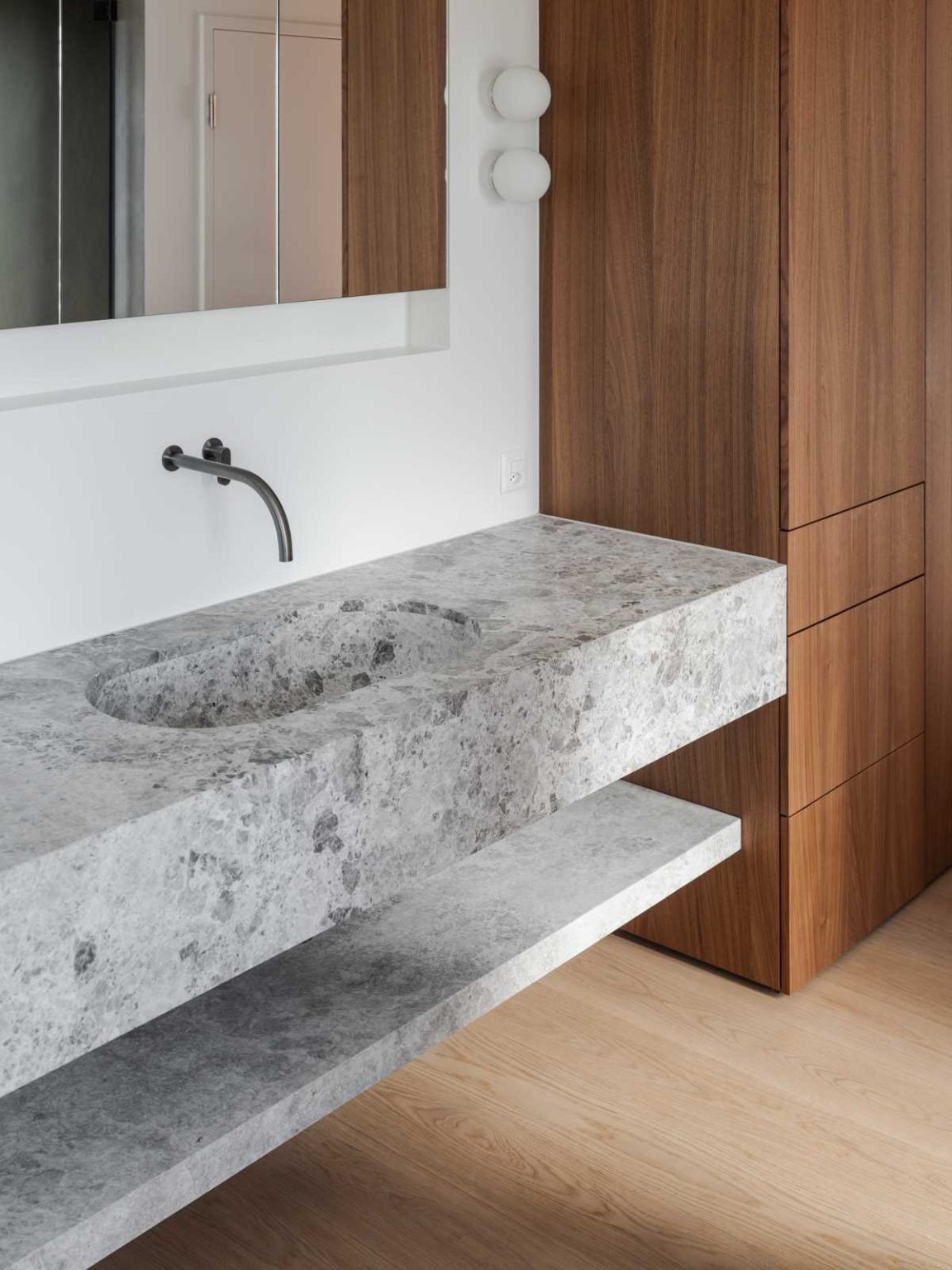 A freestanding bathtub sits on a raised platform beside the window in this elegant primary bathroom, paired with a stone vanity and warm wood cabinetry.