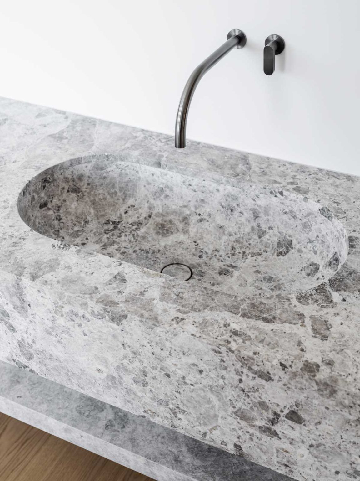 A freestanding bathtub sits on a raised platform beside the window in this elegant primary bathroom, paired with a stone vanity and warm wood cabinetry.
