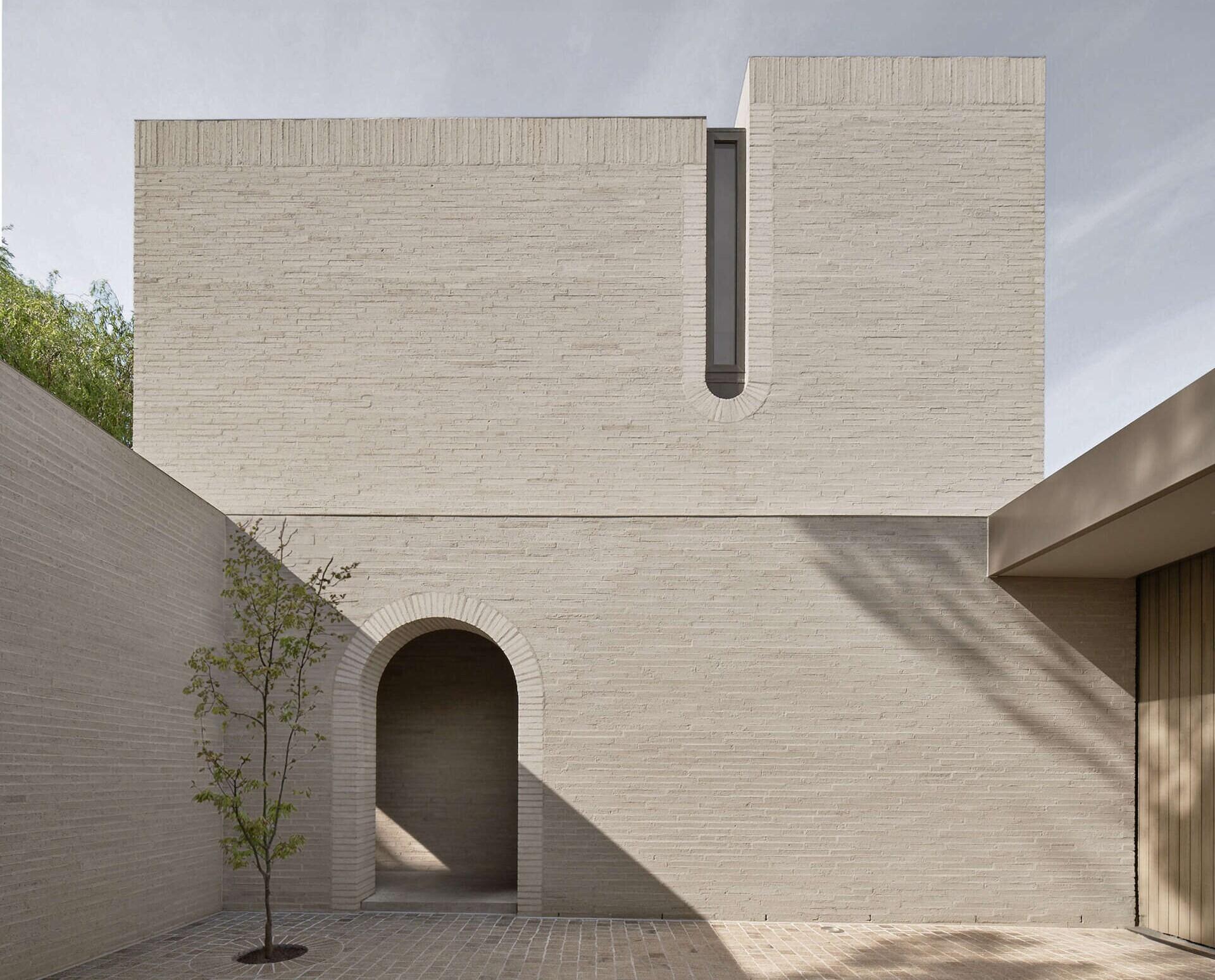 The exterior is defined by white brick, used across a facade with very few openings. From the laneway, the building appears solid and quiet. Behind that exterior, the architecture becomes increasingly layered, balancing rational planning with brick, timber, travertine, planting, textiles, art and collected objects.