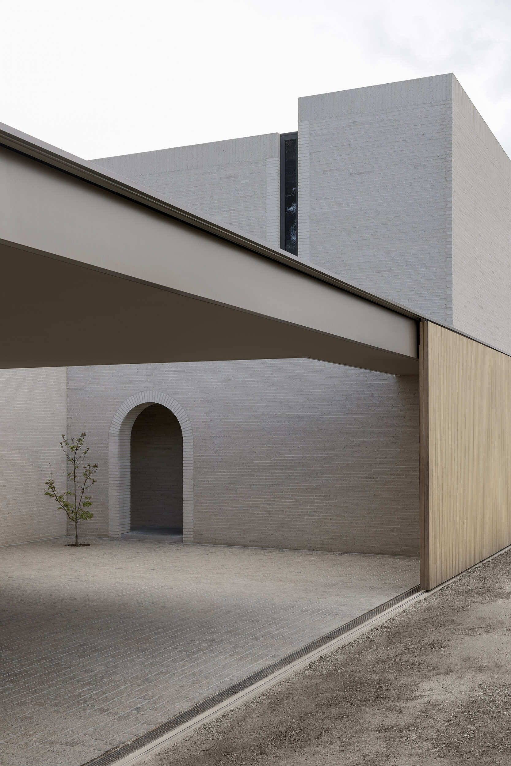 The exterior is defined by white brick, used across a facade with very few openings. From the laneway, the building appears solid and quiet. Behind that exterior, the architecture becomes increasingly layered, balancing rational planning with brick, timber, travertine, planting, textiles, art and collected objects.
