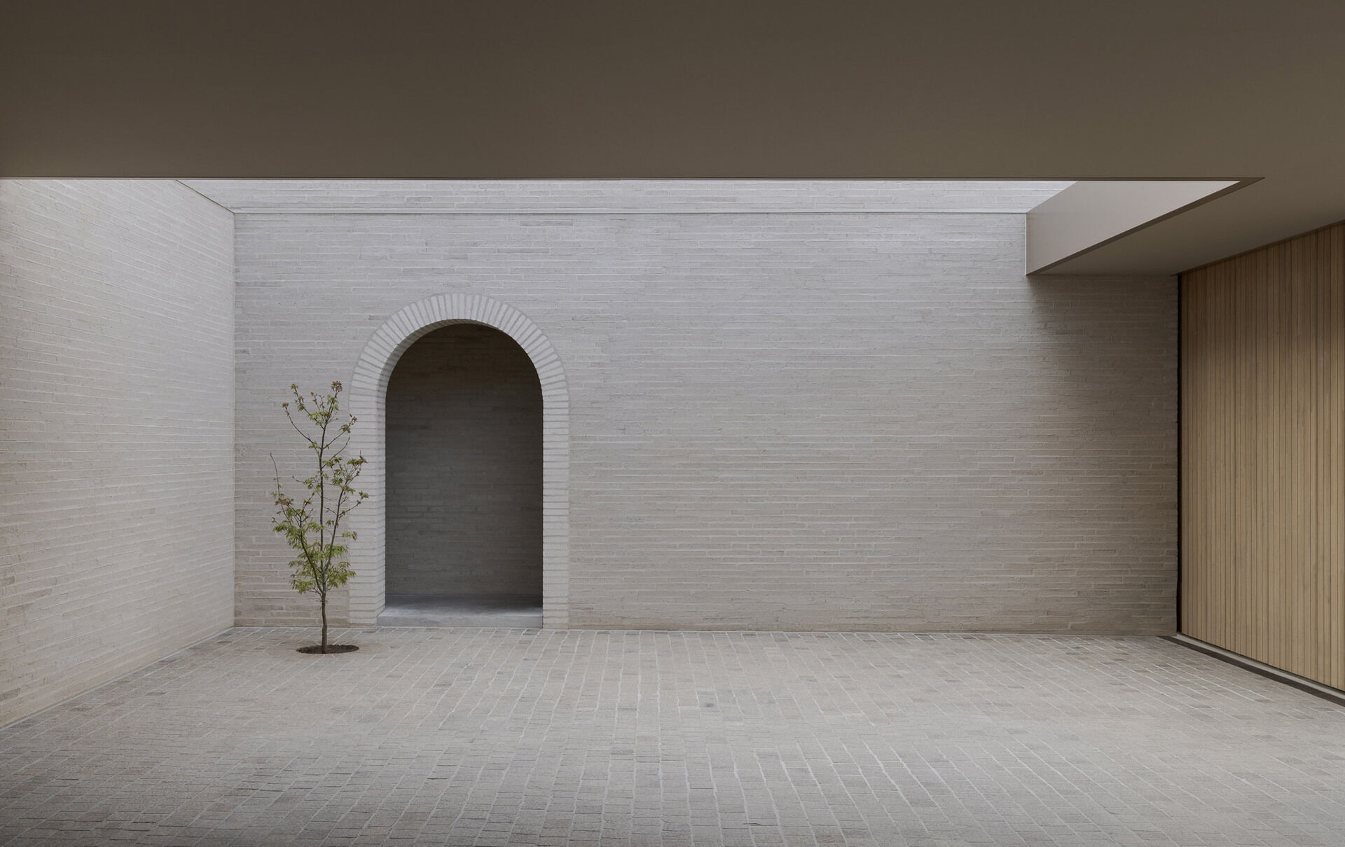The exterior is defined by white brick, used across a facade with very few openings. From the laneway, the building appears solid and quiet. Behind that exterior, the architecture becomes increasingly layered, balancing rational planning with brick, timber, travertine, planting, textiles, art and collected objects.